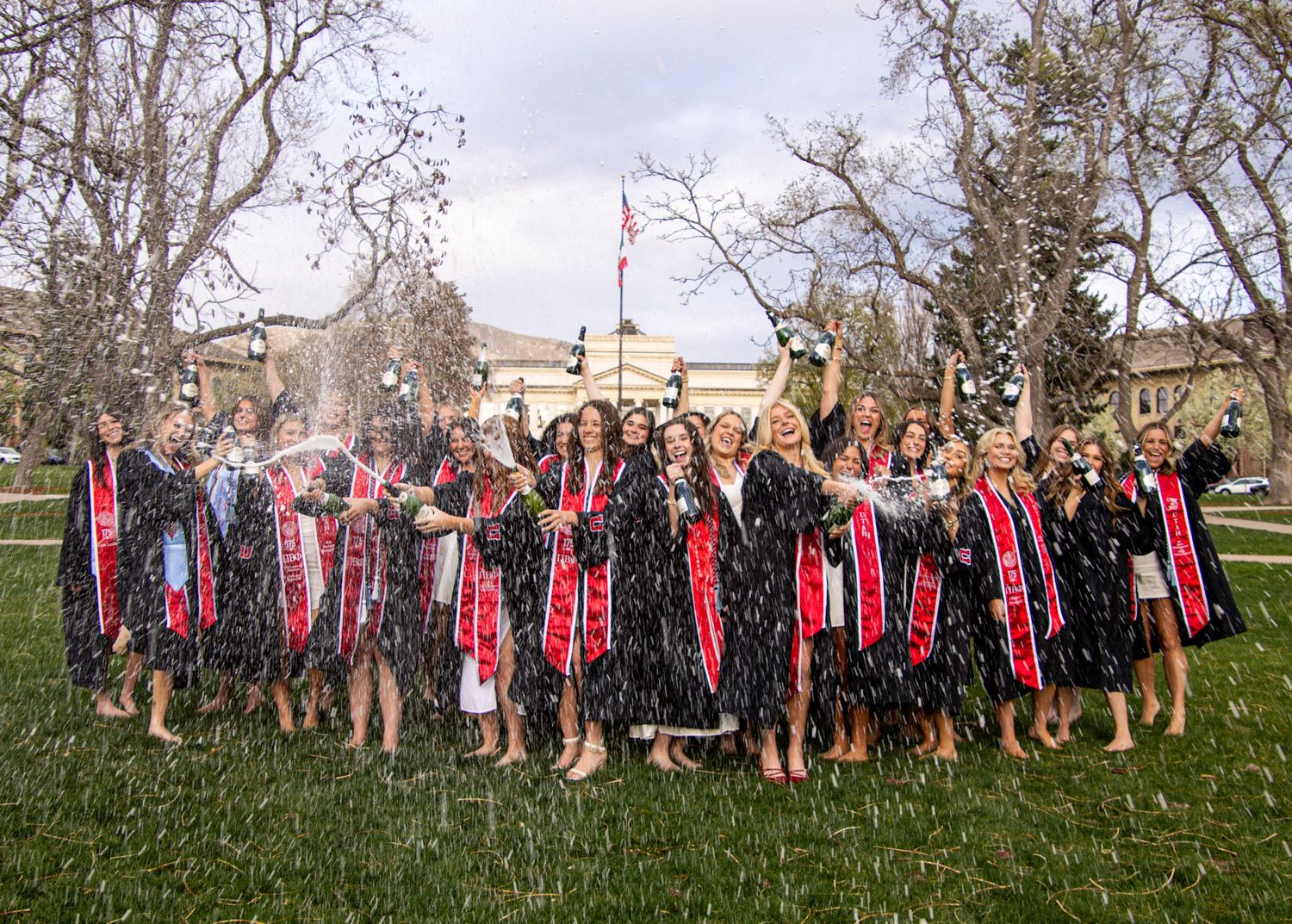 Group photo lineup in a grassy field with bare trees and cloudy sky backdrop.