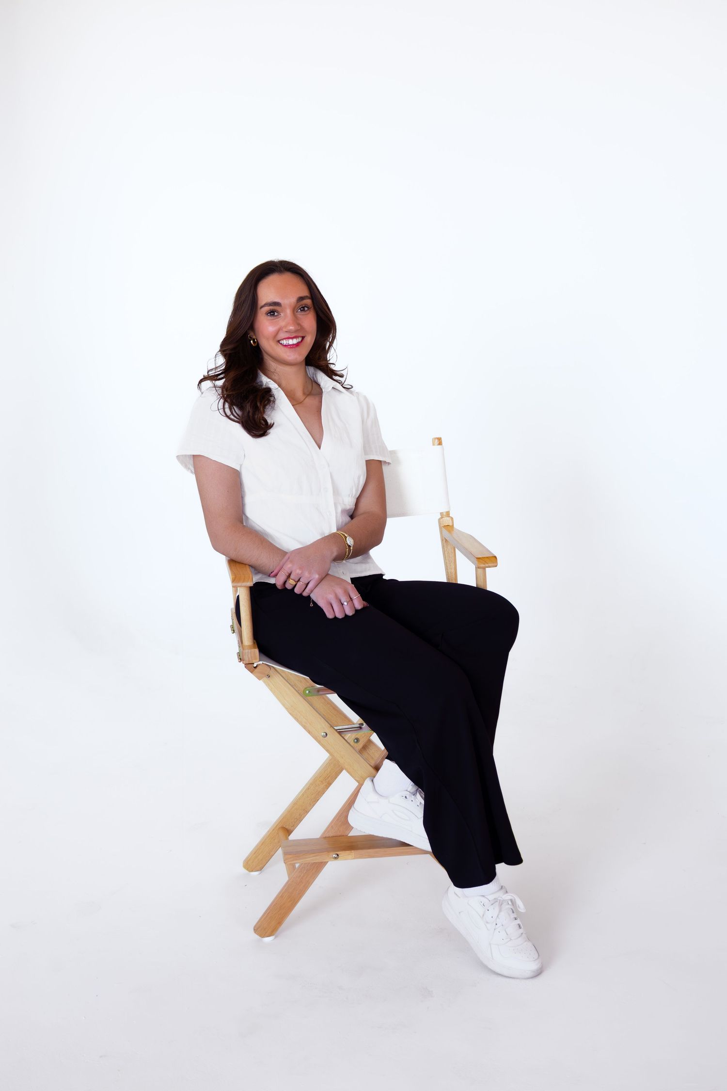 Lifestyle photo series showing casual outfit with white top and black pants while sitting in director's chair.