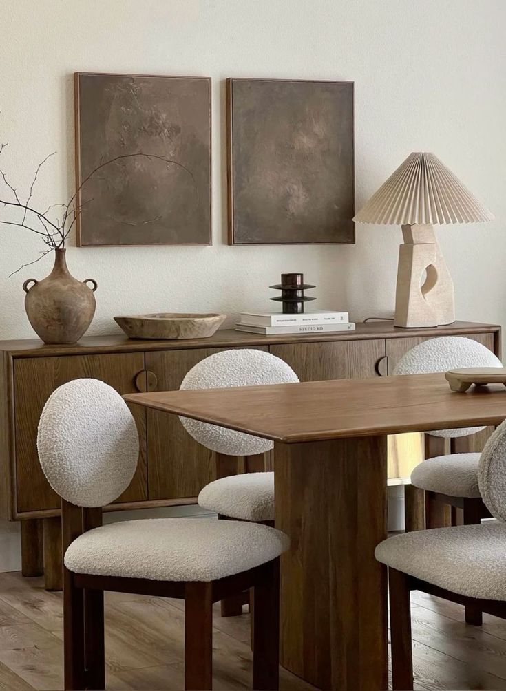 Modern dining room with wooden table and white upholstered chairs featuring minimalist wall art and spherical pendant lamps.