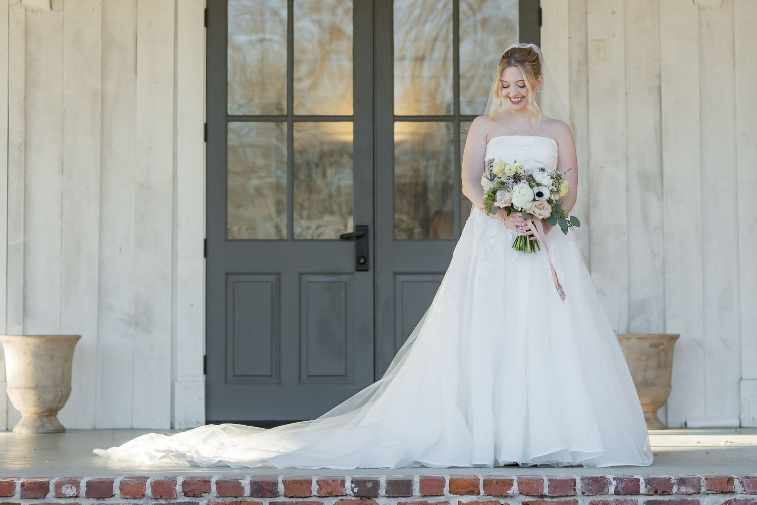 A bride gently smiling while holding her bouquet. Image by Emily Joy, wedding photographer in Memphis.