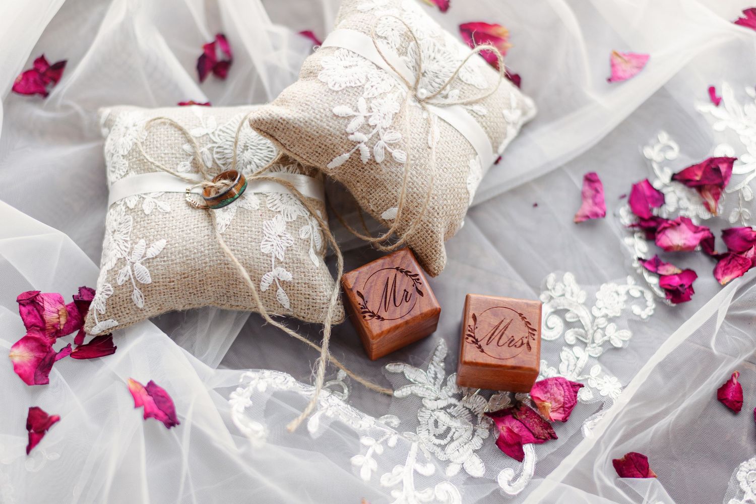 Two ring boxes with ring-bearer pillows are surrounded by tulle and rose petals. Image by Emily Joy, wedding photographer in Memphis, TN.