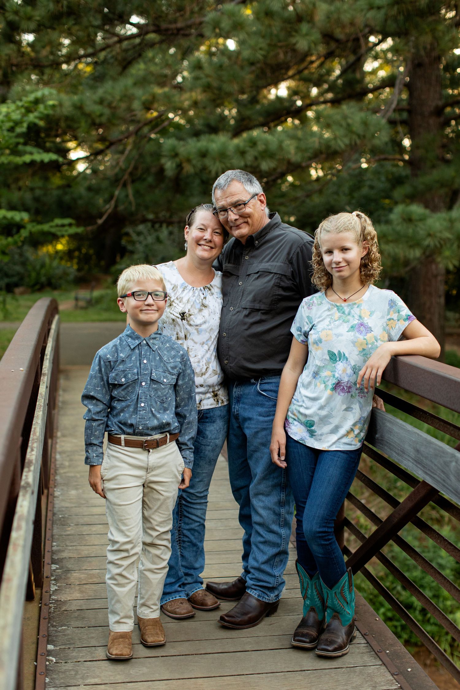 Family of four stands on a bridge and smies for a portrait by Emily Joy Photography, now a wedding photographer in Memphis, TN.