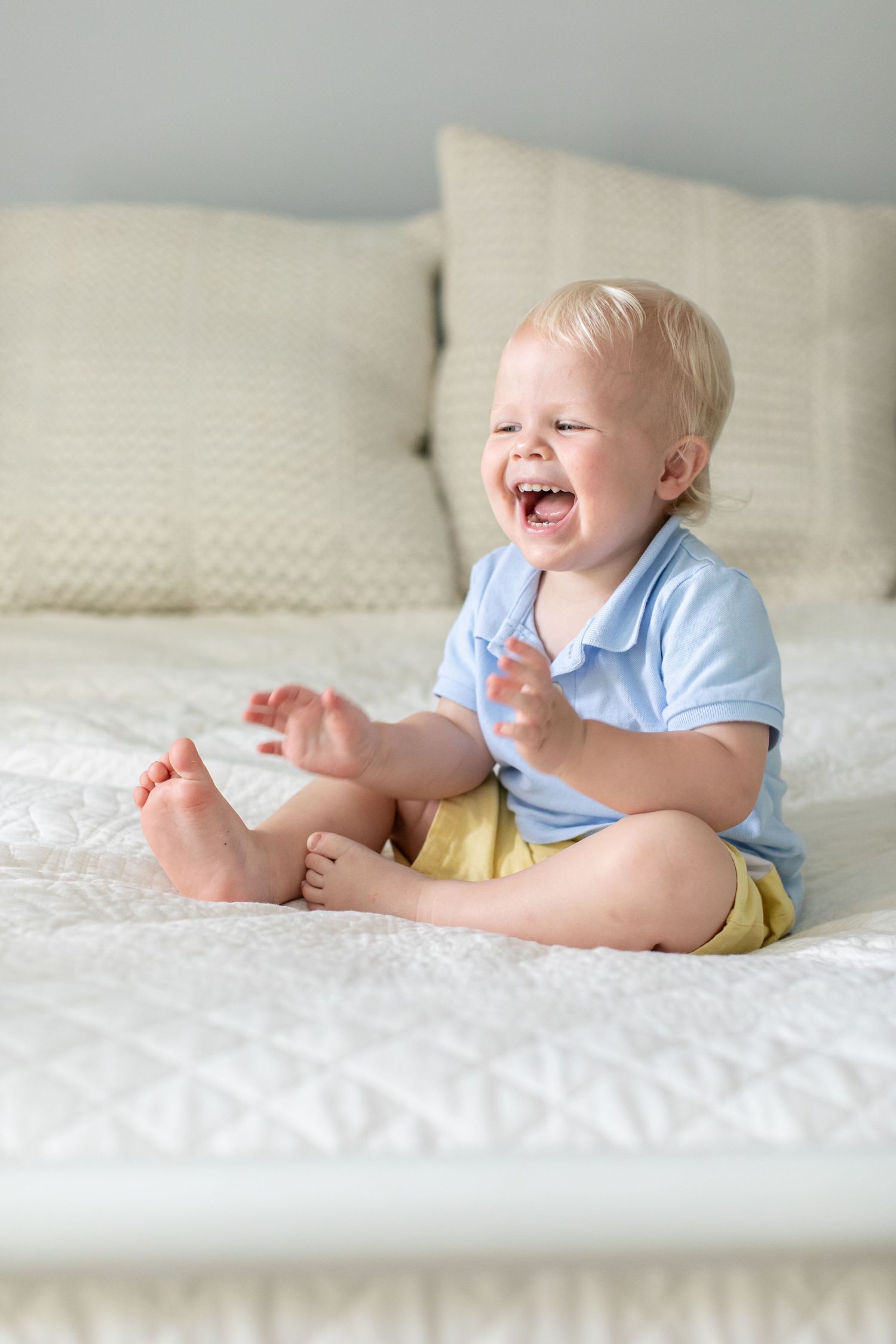 A toddler boy sitting on a bed laughs and claps for a portrait by Emily Joy Photography, now a wedding photographer in Memphis, TN.