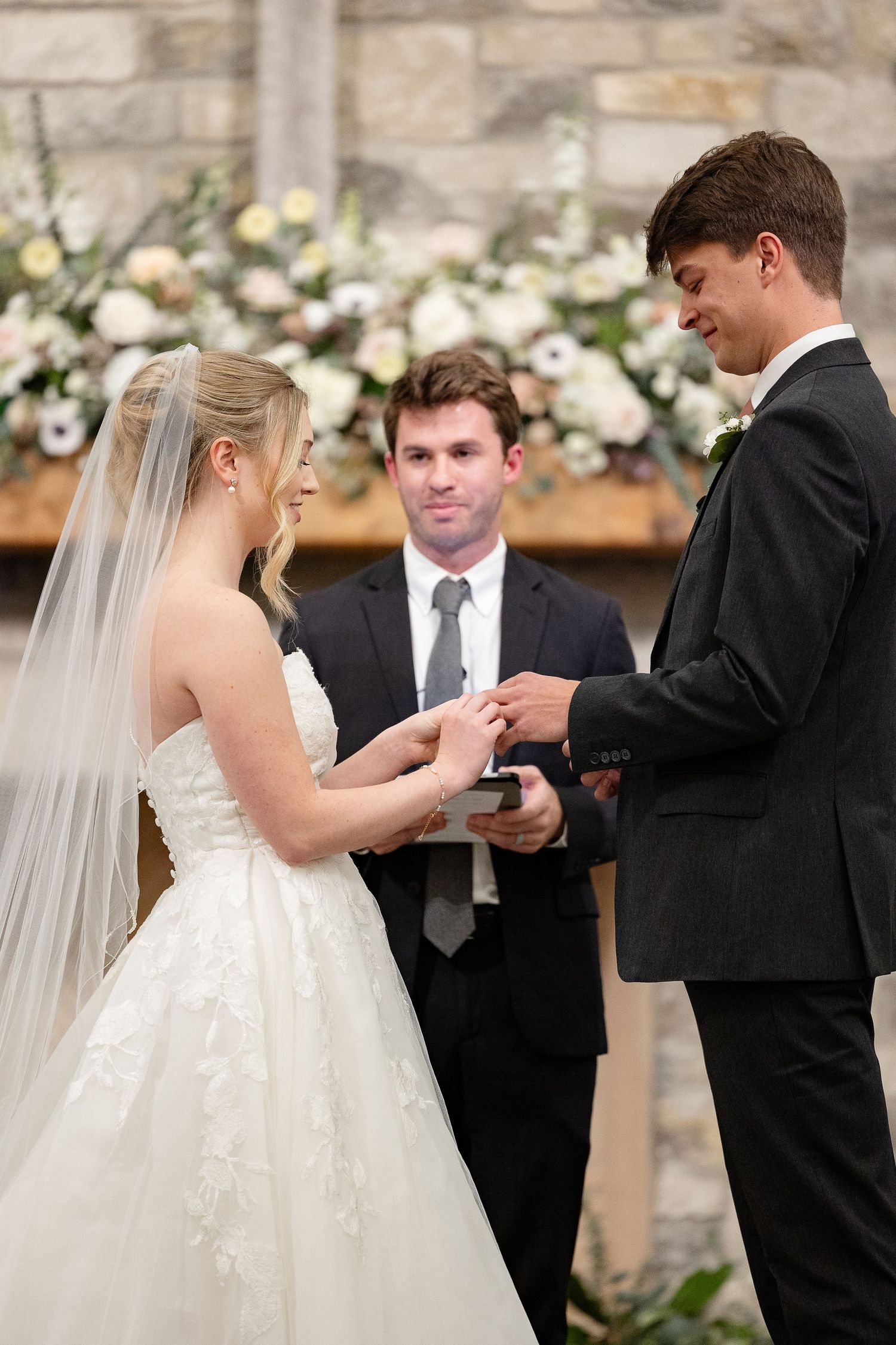 A bride places wedding ring on her groom's finger, while they both smile. Image by Emily Joy, wedding photographer in Memphis.
