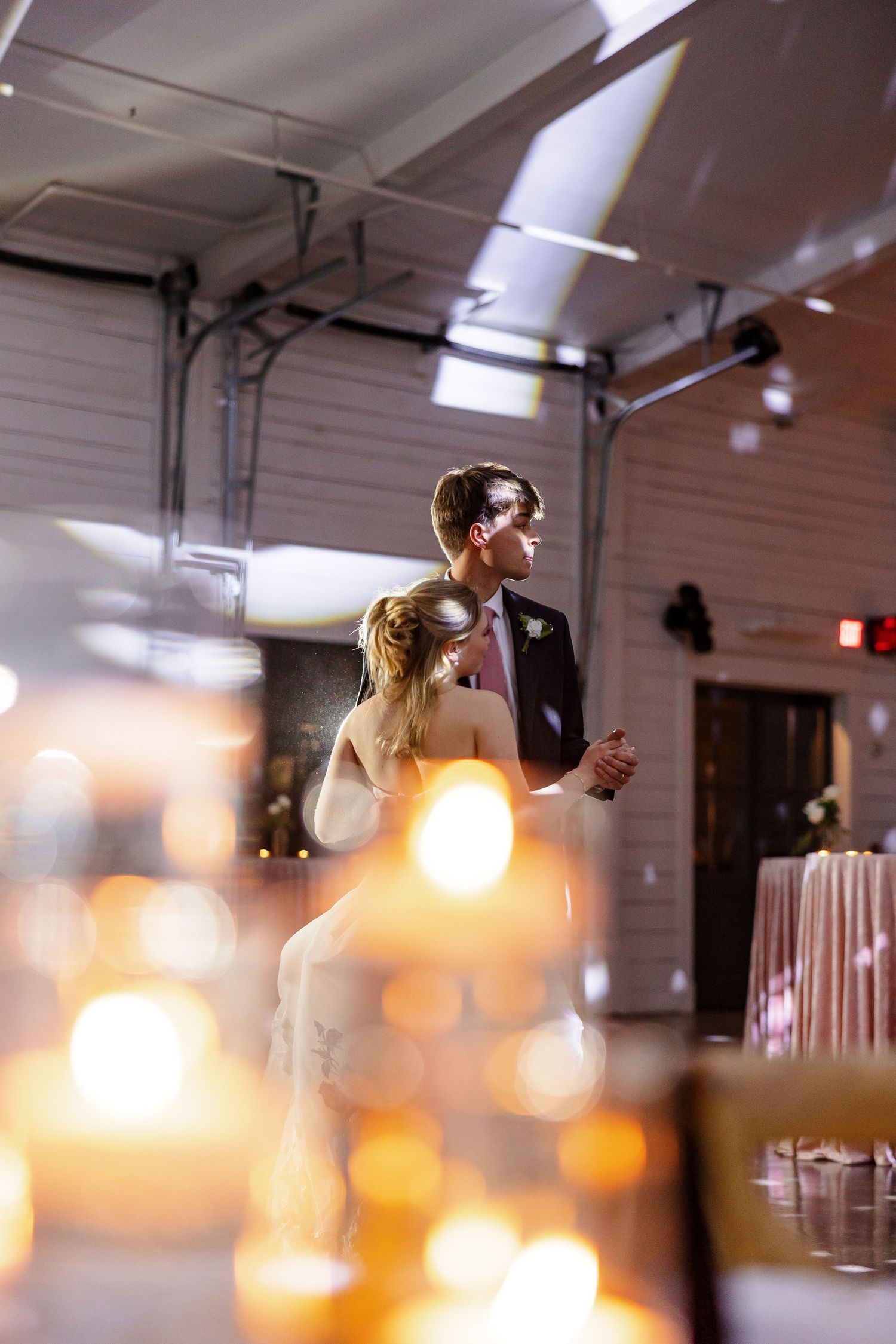 Ambiant lights blur in the foreground while bride and groom share a last dance before their exit.