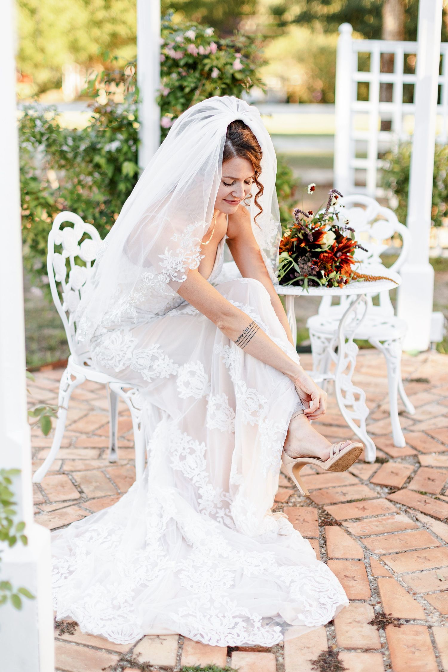 A bride in a gown and veil fastens her shoe. Image by Emily Joy, wedding photographer in Memphis.
