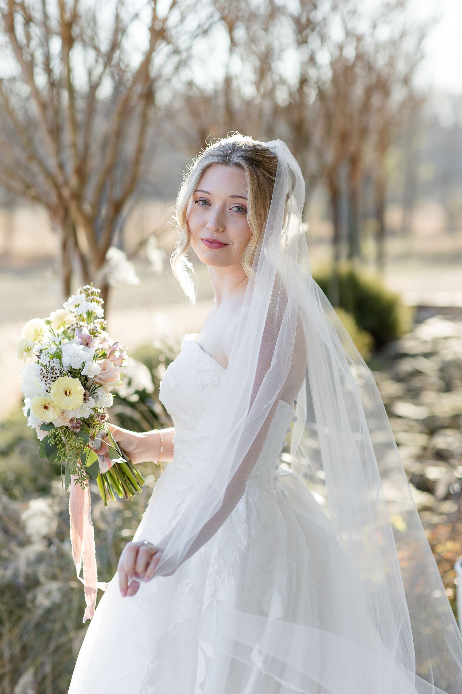 A brilliantly backlit portrait of a dazzling bride with a long veil and an a colorful bouquet outside the Robinshaw wedding venue.