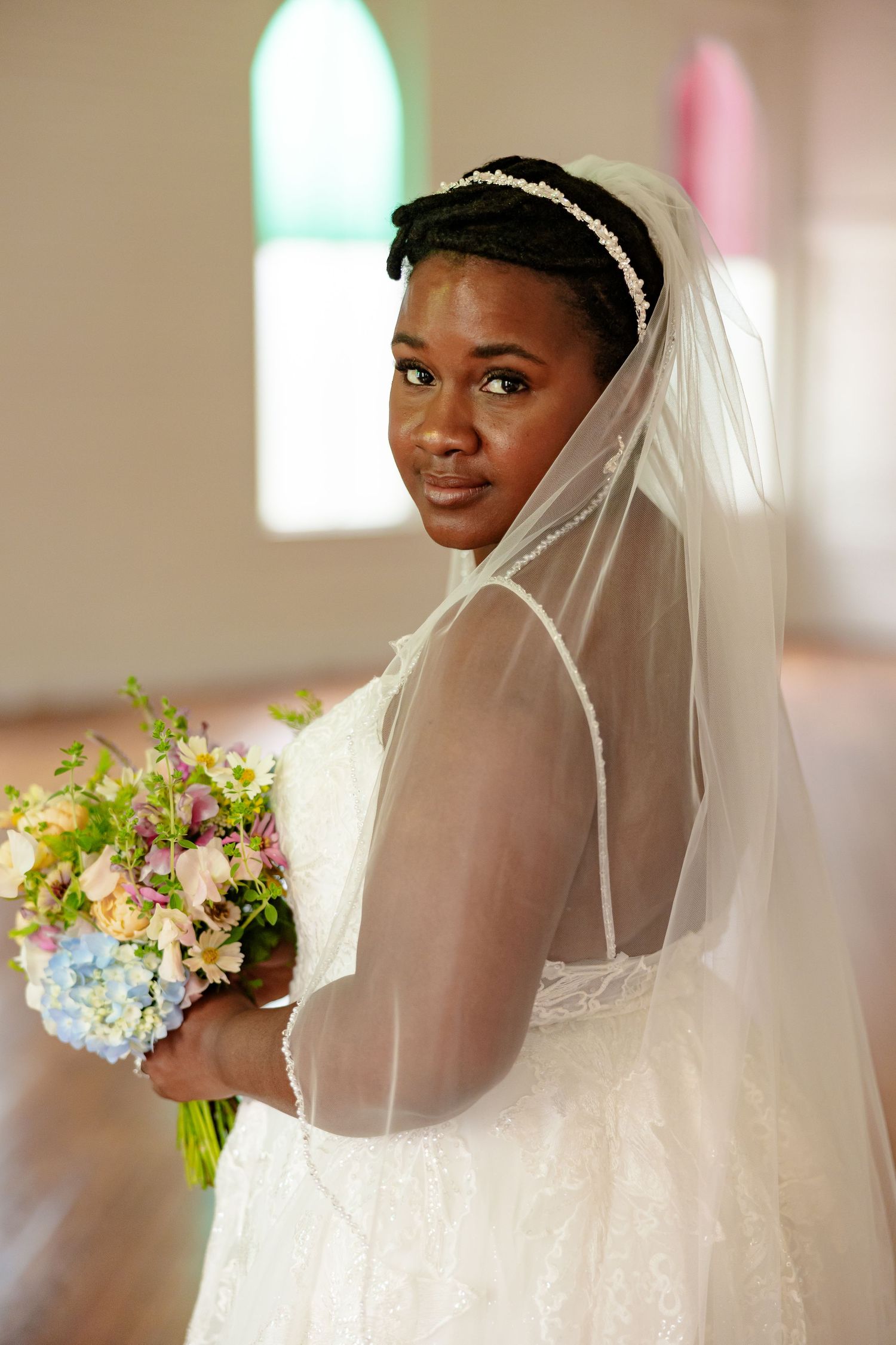 Bride with a colorful bouquet poses with stain-glassed windows  for a portrait by Memphis Wedding Photographer Emily Joy Photography