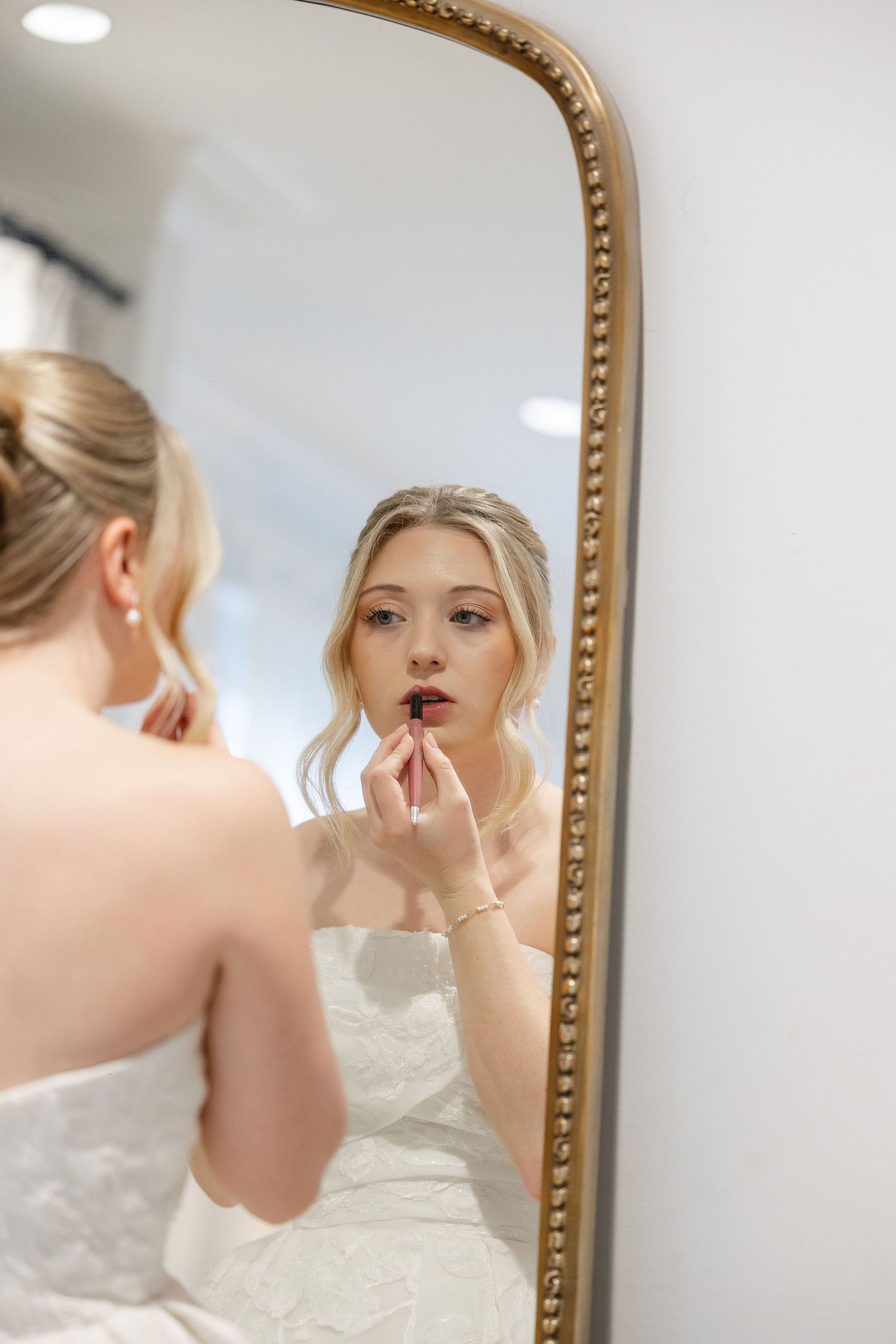 Candid portrait shot through a mirror in the bride's room at the Robinshaw wedding venue, showing  a beautiful bride re-touching her makeup.