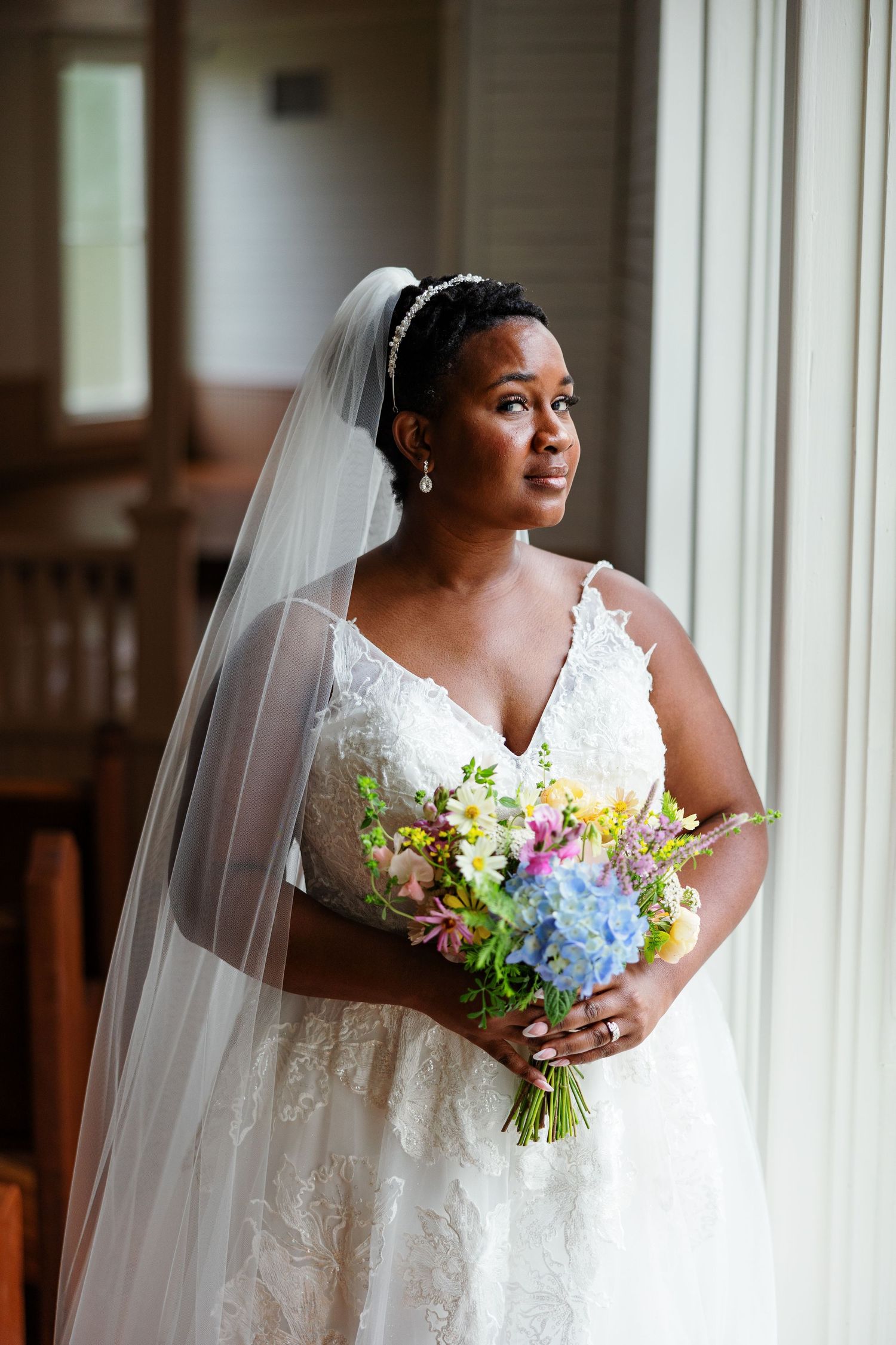 A bride in an elegant gown stands by a window for portrait by Memphis Wedding Photographer Emily Joy Photography