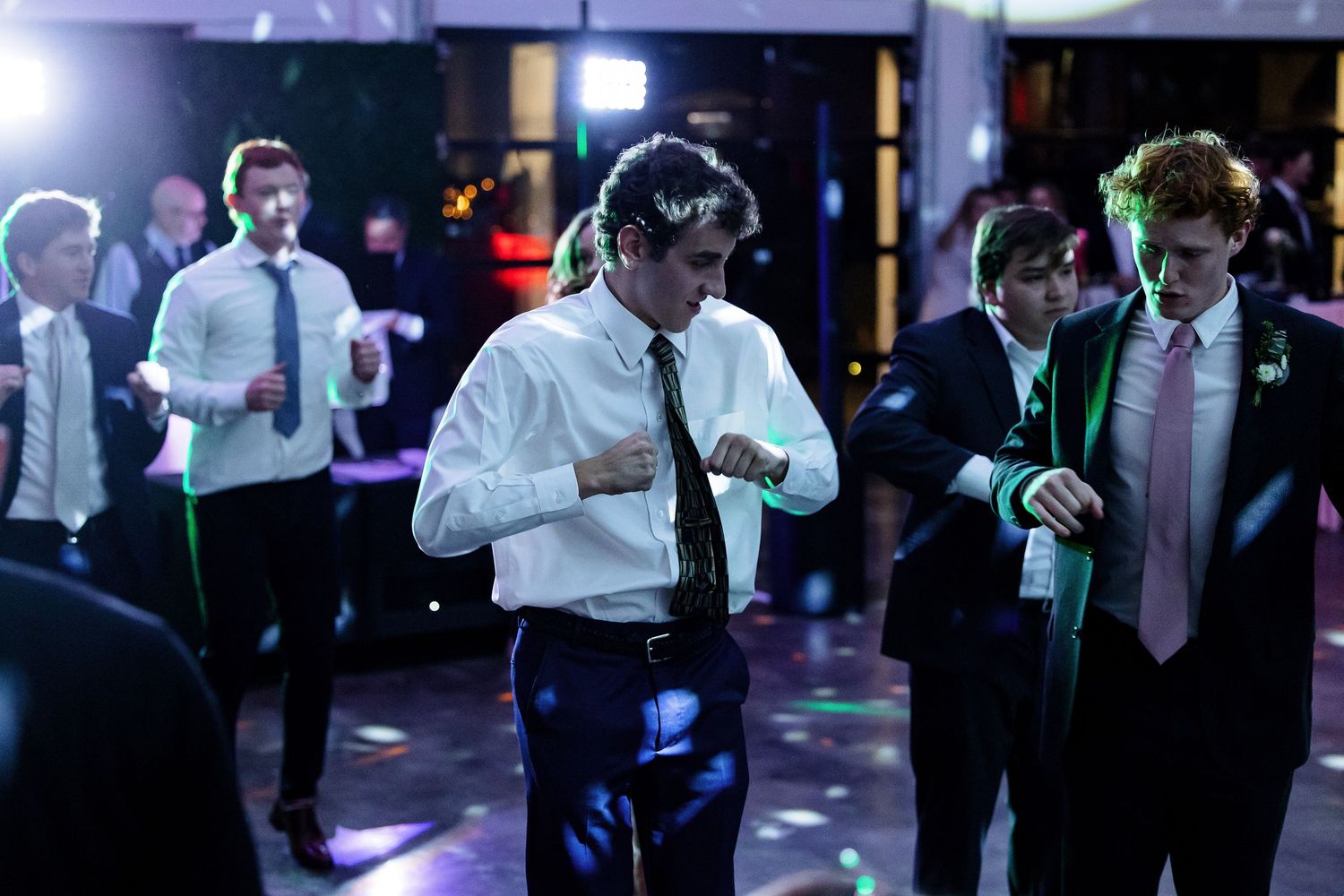 A group of reception guests enjoy party dancing with colorful lights and disco ball. Image by Emily Joy, wedding photographer in Memphis.