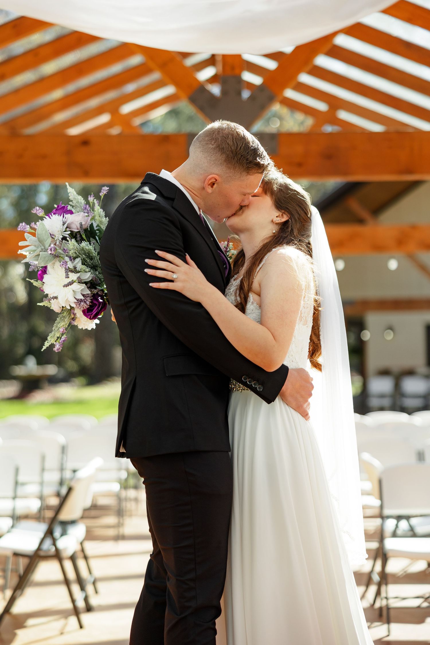 A bride and groom kiss under the awning of the outdoor ceremony structure.