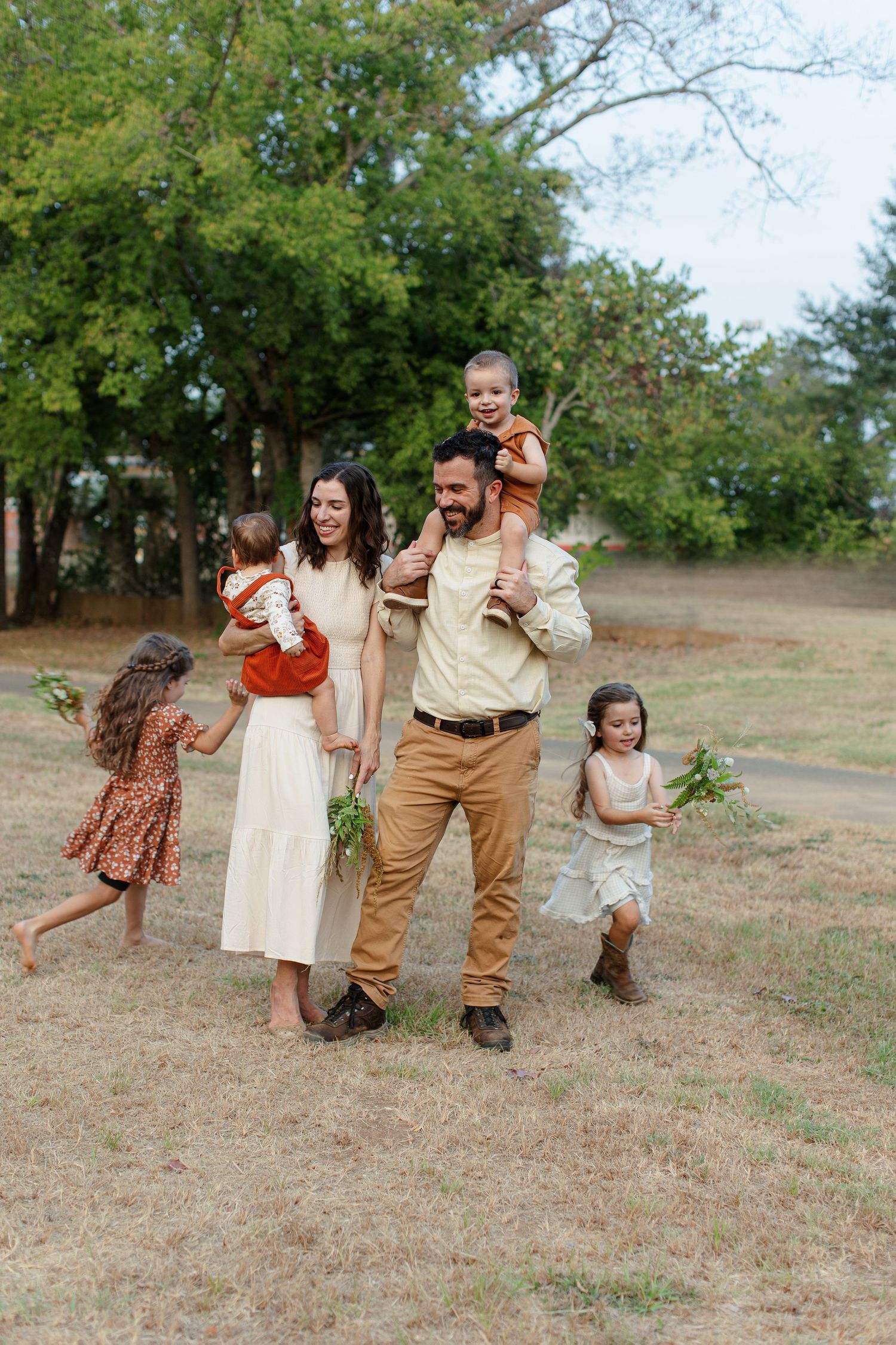 A couple holds a toddler and baby while two girls run around for a portrait by Emily Joy Photography, now a wedding photographer in Memphis.