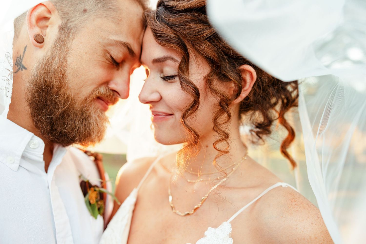 An under-the-veil shot of the bride and groom, smiling peacefully with closed eyes. Image by Emily Joy, wedding photographer in Memphis.