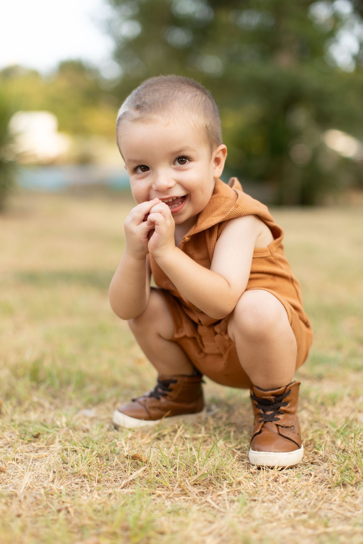 A toddler boy crouches and smiles for a portrait  by Emily Joy Photography, now a wedding photographer in Memphis, TN.