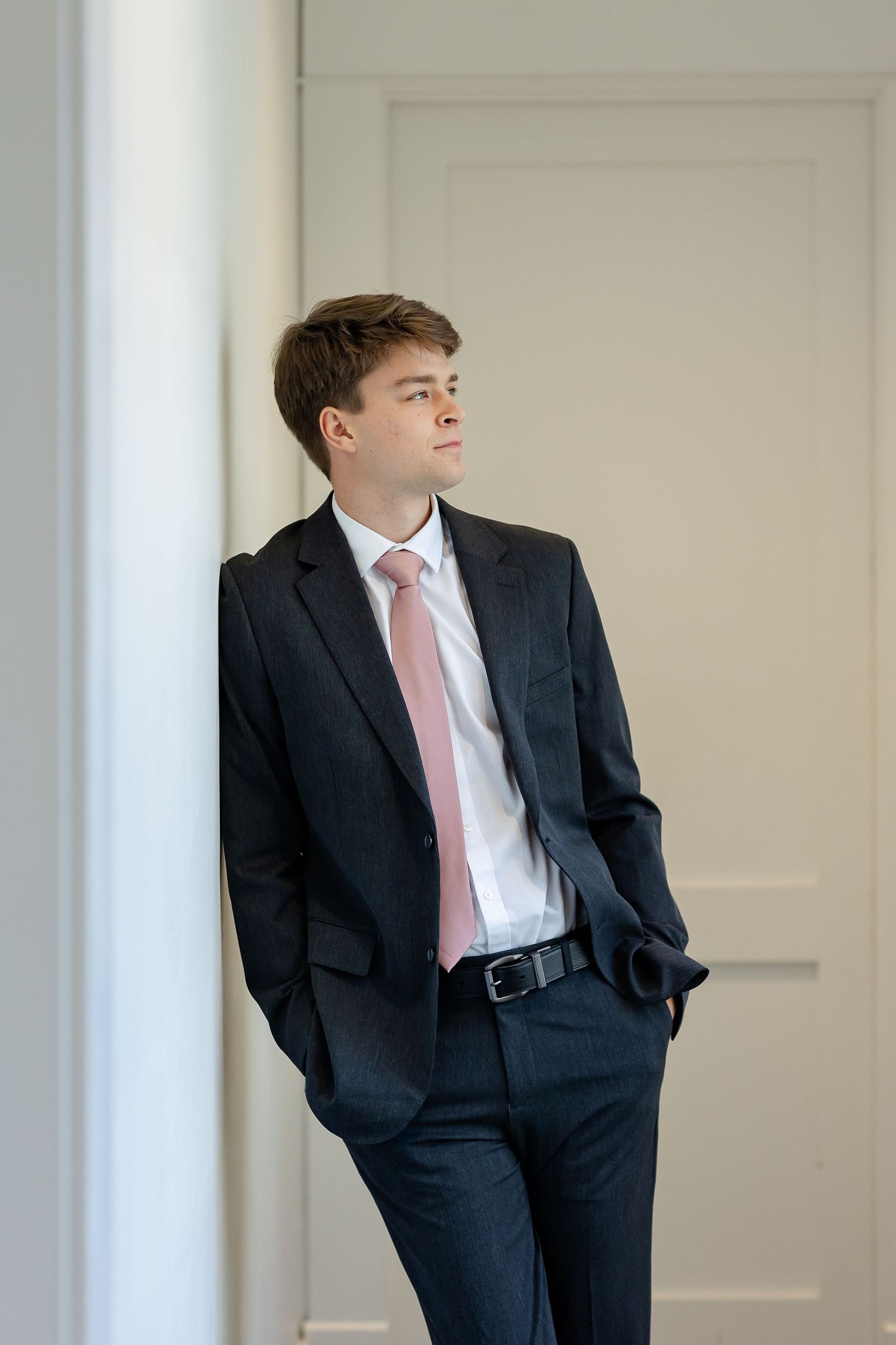 A handsome young groom looks out a window for a candid portrait by Memphis wedding photographer, Emily Joy Photography.