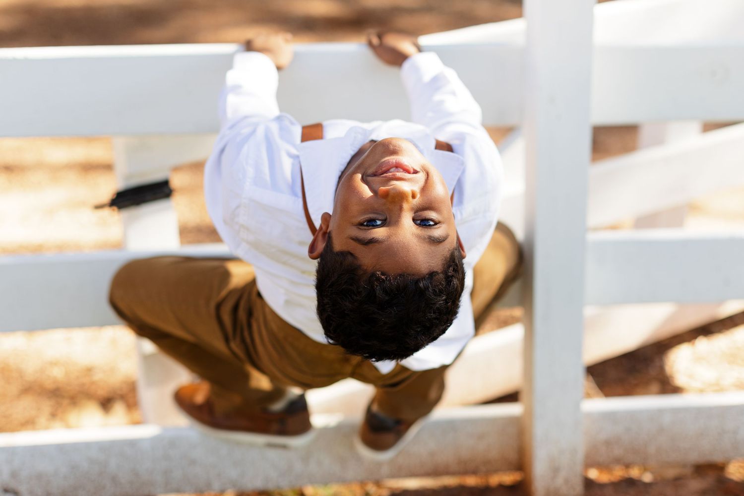 Cute young ring bearer hangs on a fence for his candid portrait.