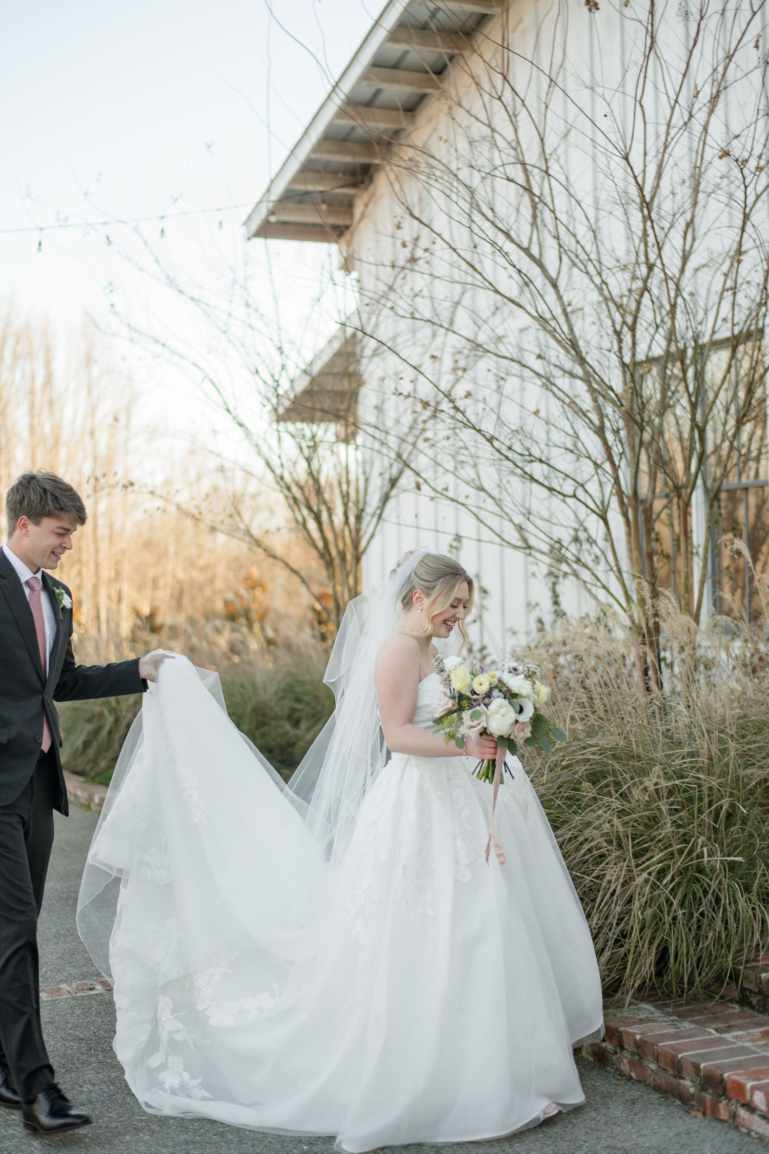 A groom hold the train of his bride's dress as they approach the stairs in front of the Robinshaw wedding venue.