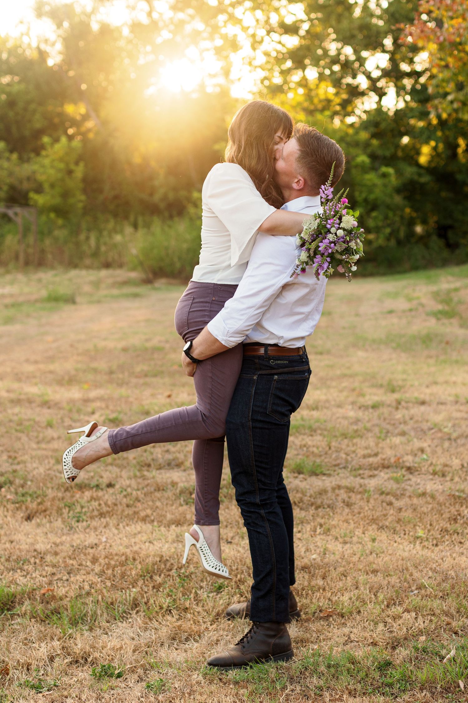 Young man lifts his bride-to-be for a kiss at sunset for a portrait by Emily Joy Photography, now a wedding photographer in Memphis, TN.