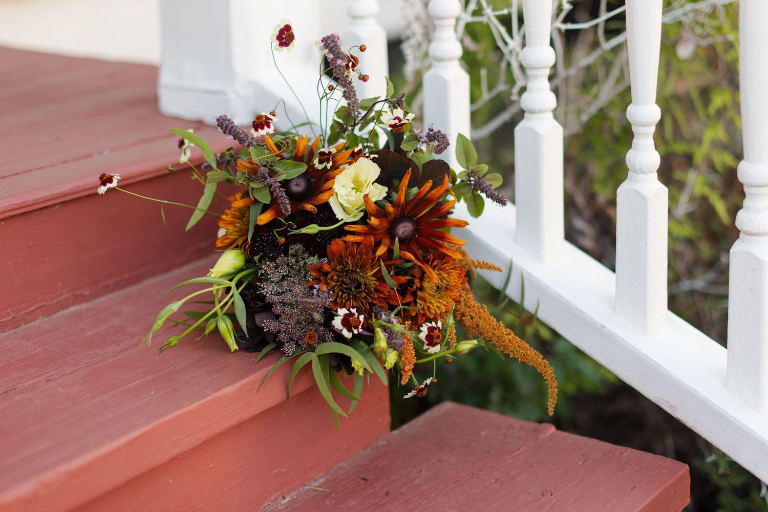 An elegant autumnal bouquet rests on a staircase by white railing.