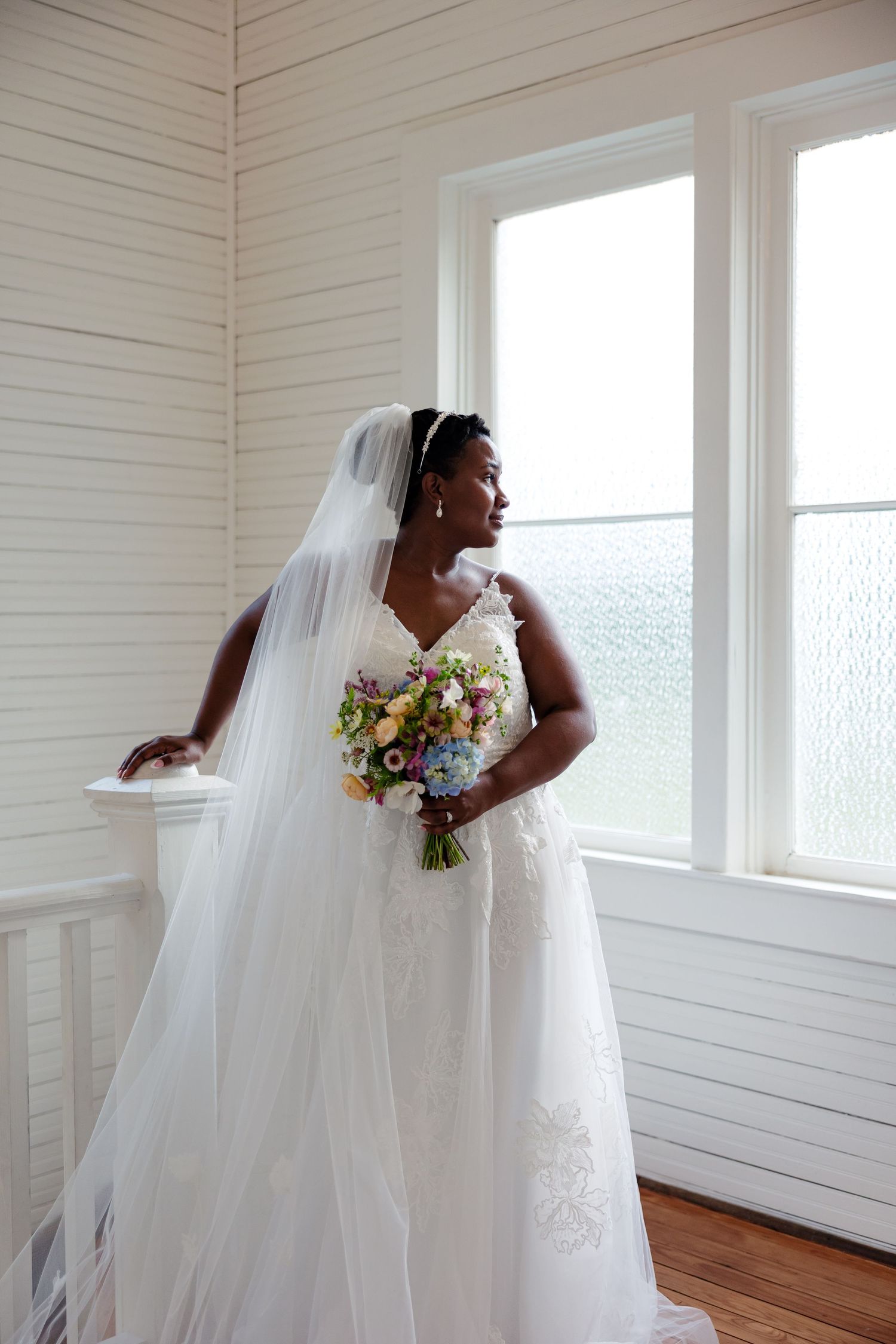 A bride in an elegant gown looks out a window for portrait by Memphis Wedding Photographer Emily Joy Photography
