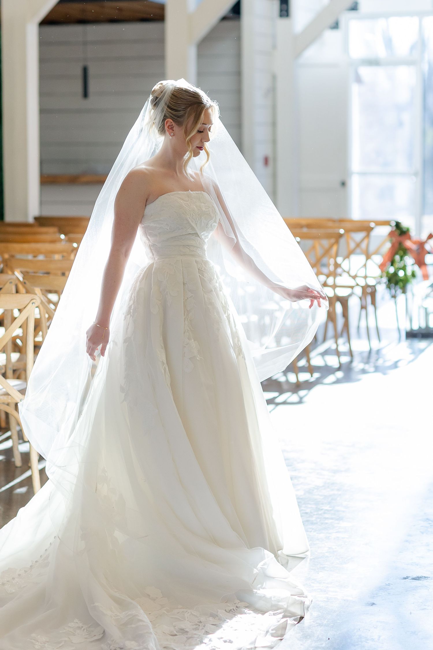 A strikingly backlit bride adjusts her veil inside a bright ceremony room. Image by Emily Joy, wedding photographer in Memphis.