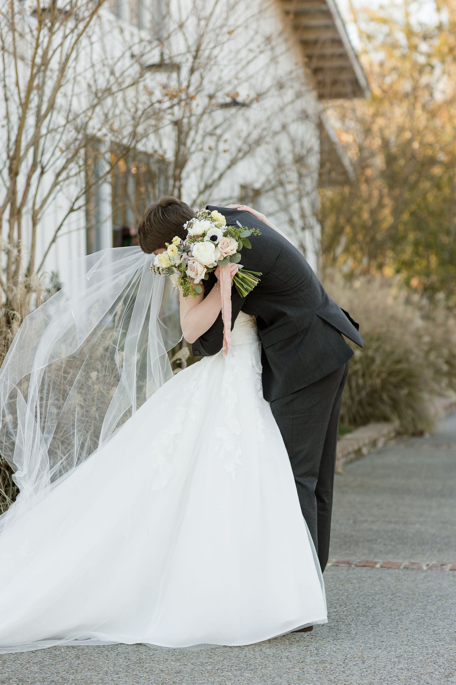 After the first look, a groom hugs his bride while her veil blows in the wind. Image by Emily Joy, wedding photographer in Memphis.