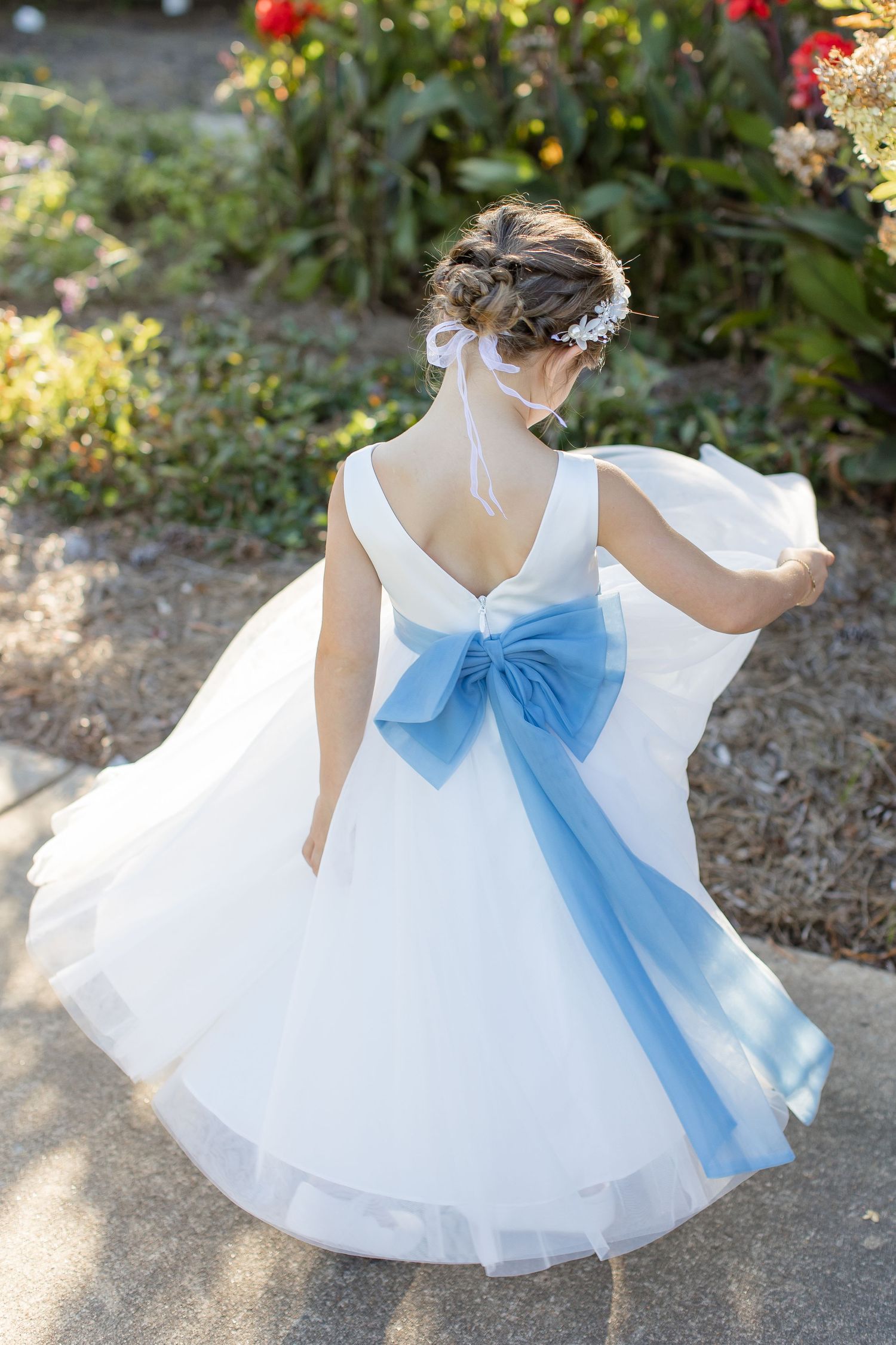 A flower girl in a while dress with a blue sash twirls in a portrait by Emily Joy Photography, wedding photographer in Memphis, TN.