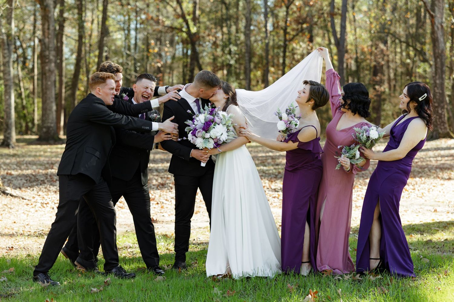 A bride and groom kiss as the wedding party teasingly try to pull them apart.