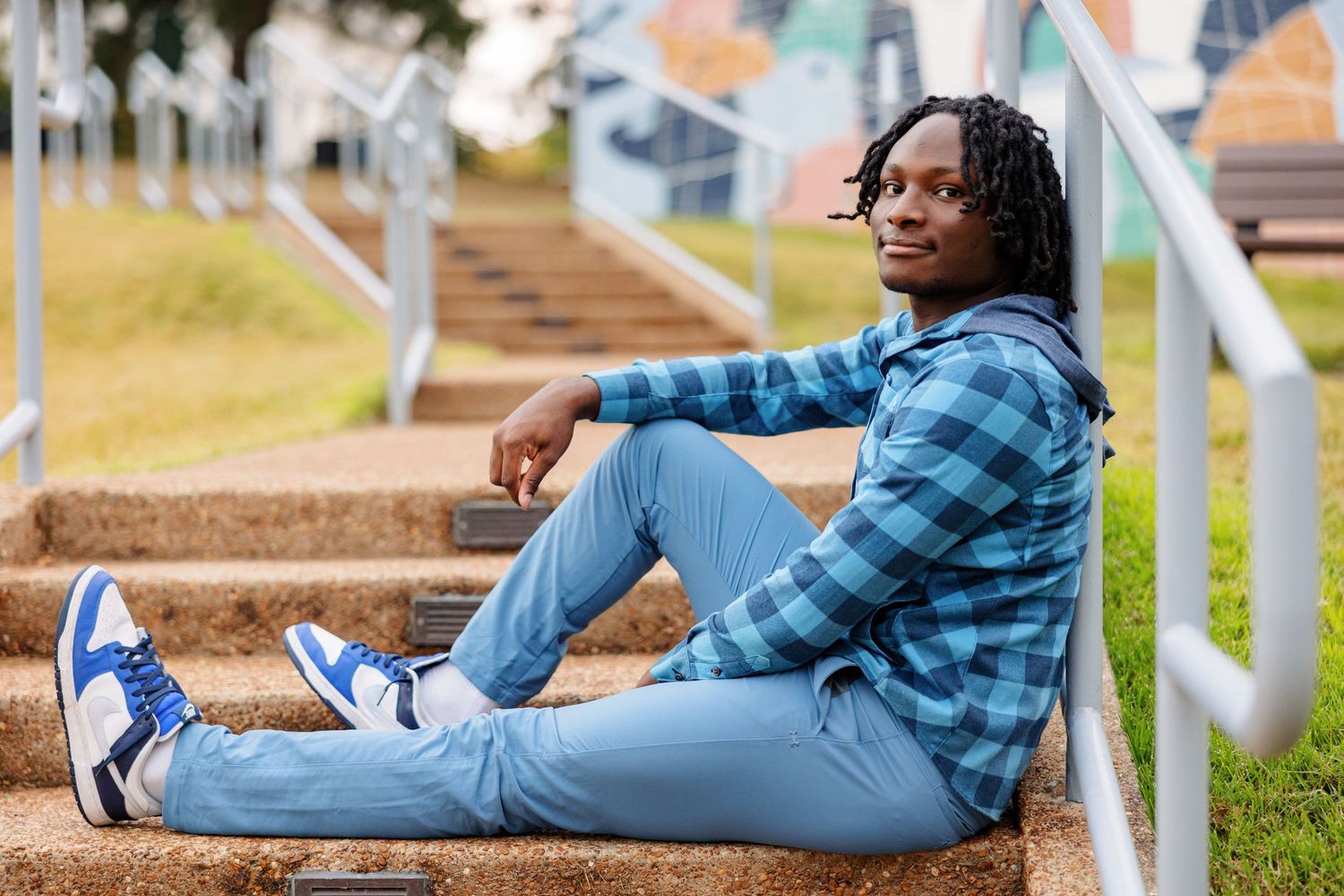 A senior boy leans back agains stair railing in an artistic pose with a painted wall behind him.
