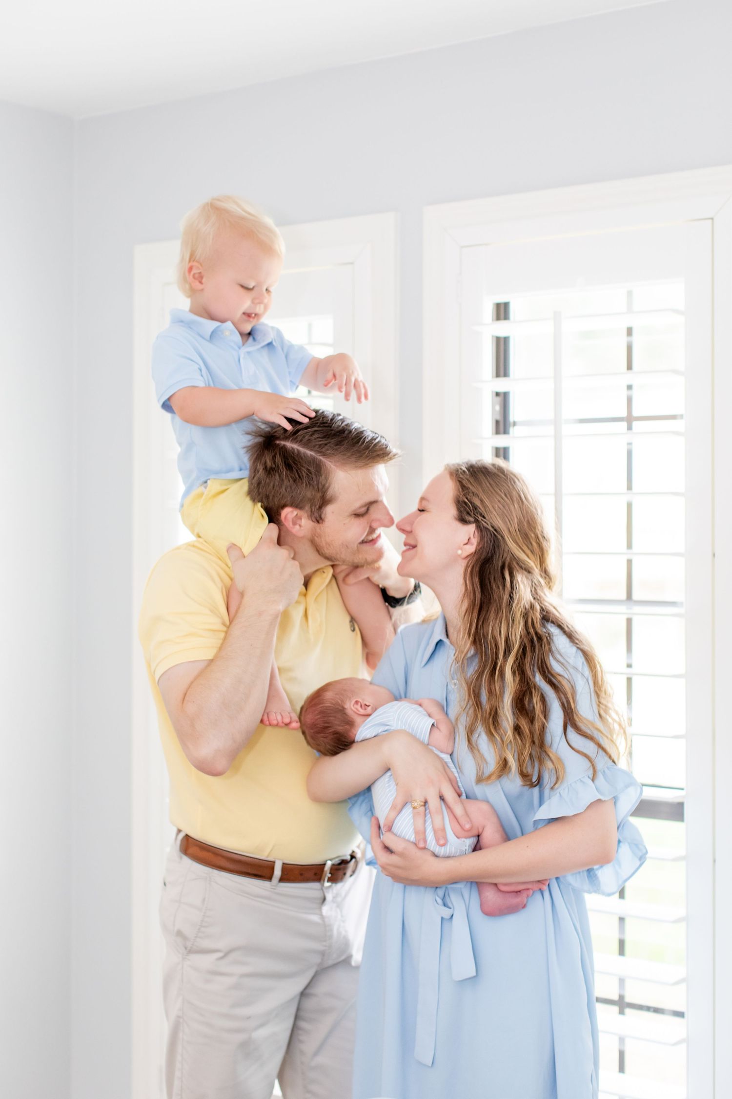 Husband and wife share a kiss as they each hold one son for a portrait by Emily Joy Photography, now a wedding photographer in Memphis, TN.