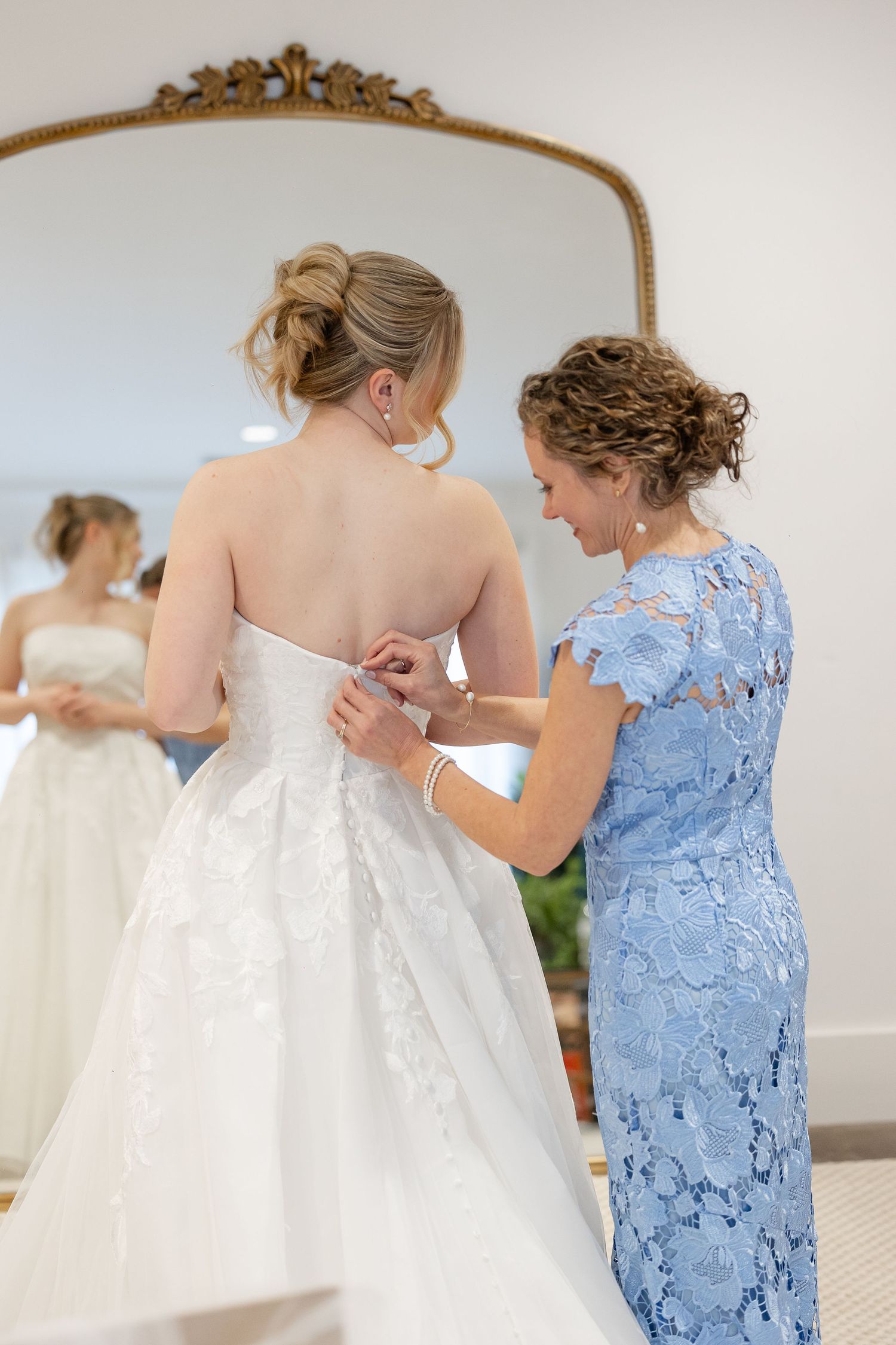 Portrait of a mother fastening the beautiful buttons on the back of her daughter's wedding dress in front of a full mirror at the Robinshaw.