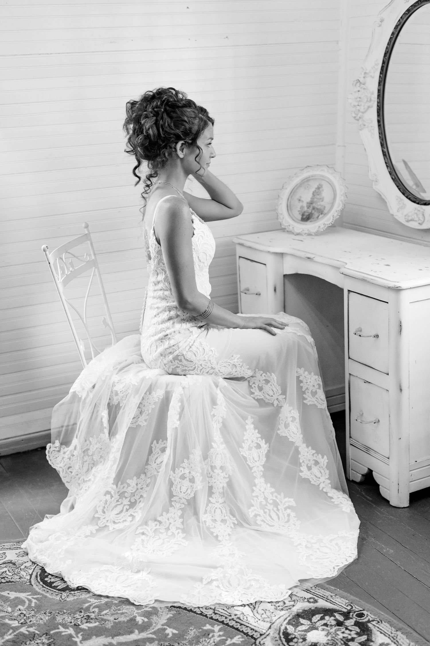 A bride adjusts her curly hair while checking her appearance in a mirror. Image by Emily Joy, wedding photographer in Memphis.