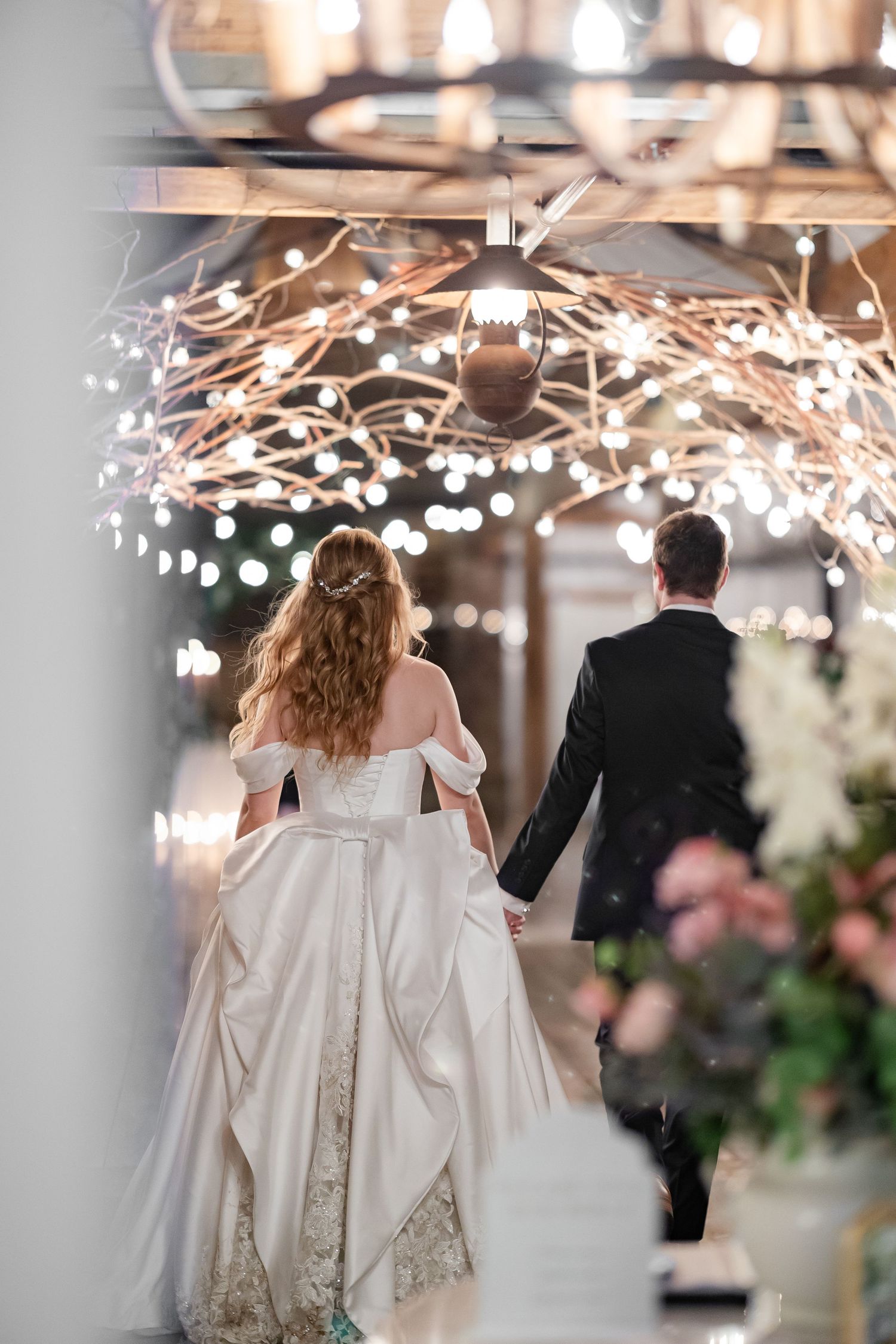 A newly married couple walks under a light arch to enter their reception, image by Emily Joy, wedding photographer in Memphis.