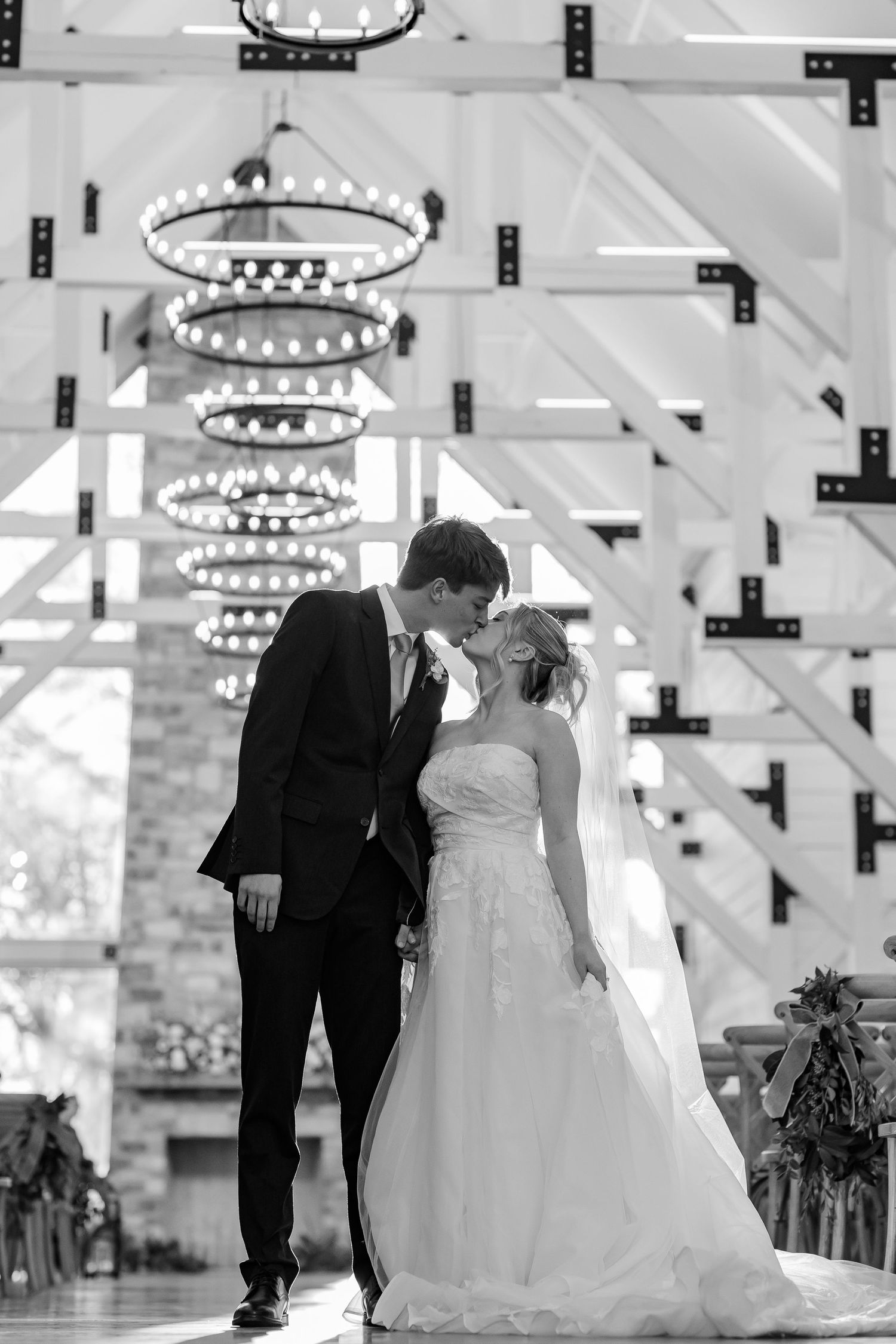A portrait featuring a bride and groom kissing while standing under chandeliers in the Robinshaw wedding venue.