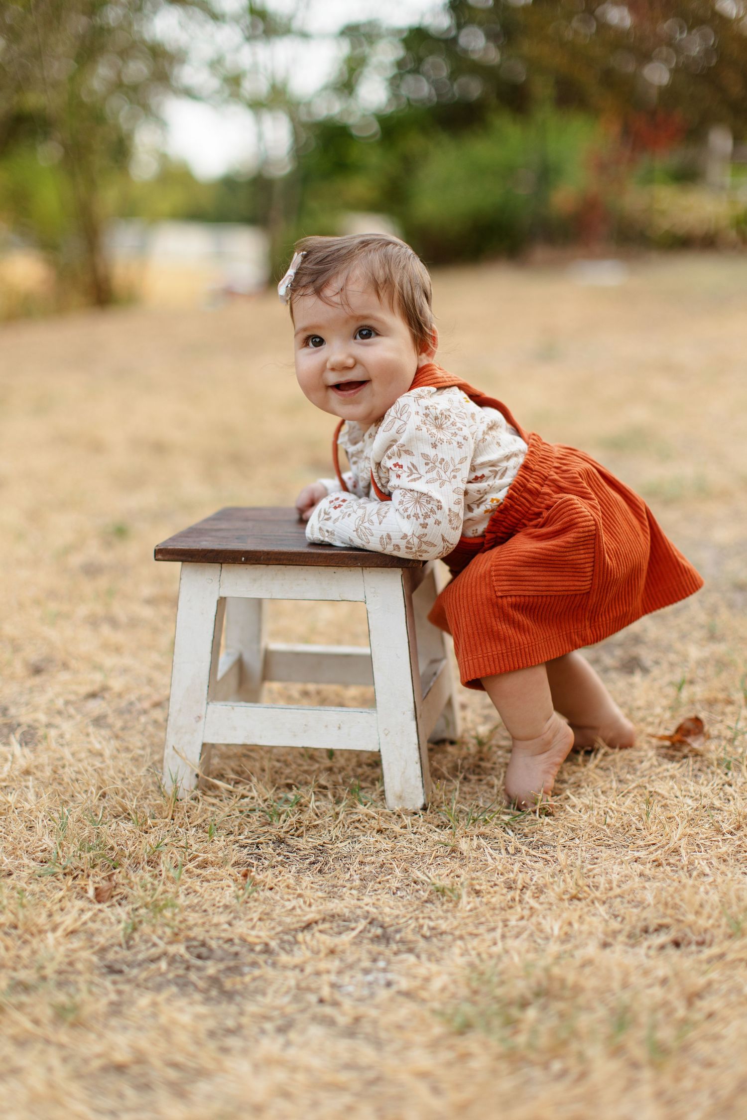 A baby girl props herself on a stool and smiles for a portrait  by Emily Joy Photography, now a wedding photographer in Memphis, TN.