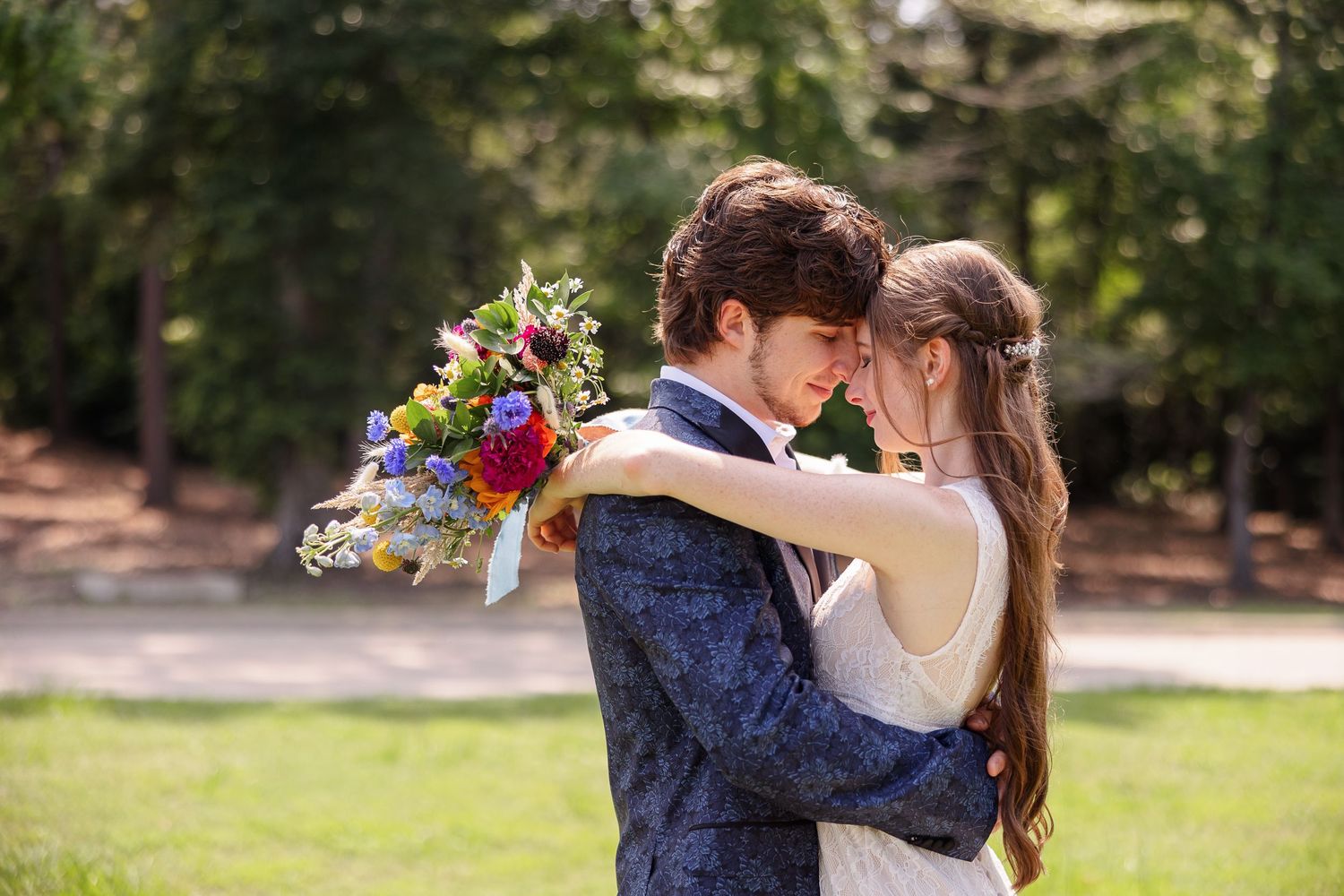 A bride and groom hug with faces together while she holds her brightly colored bouquet.