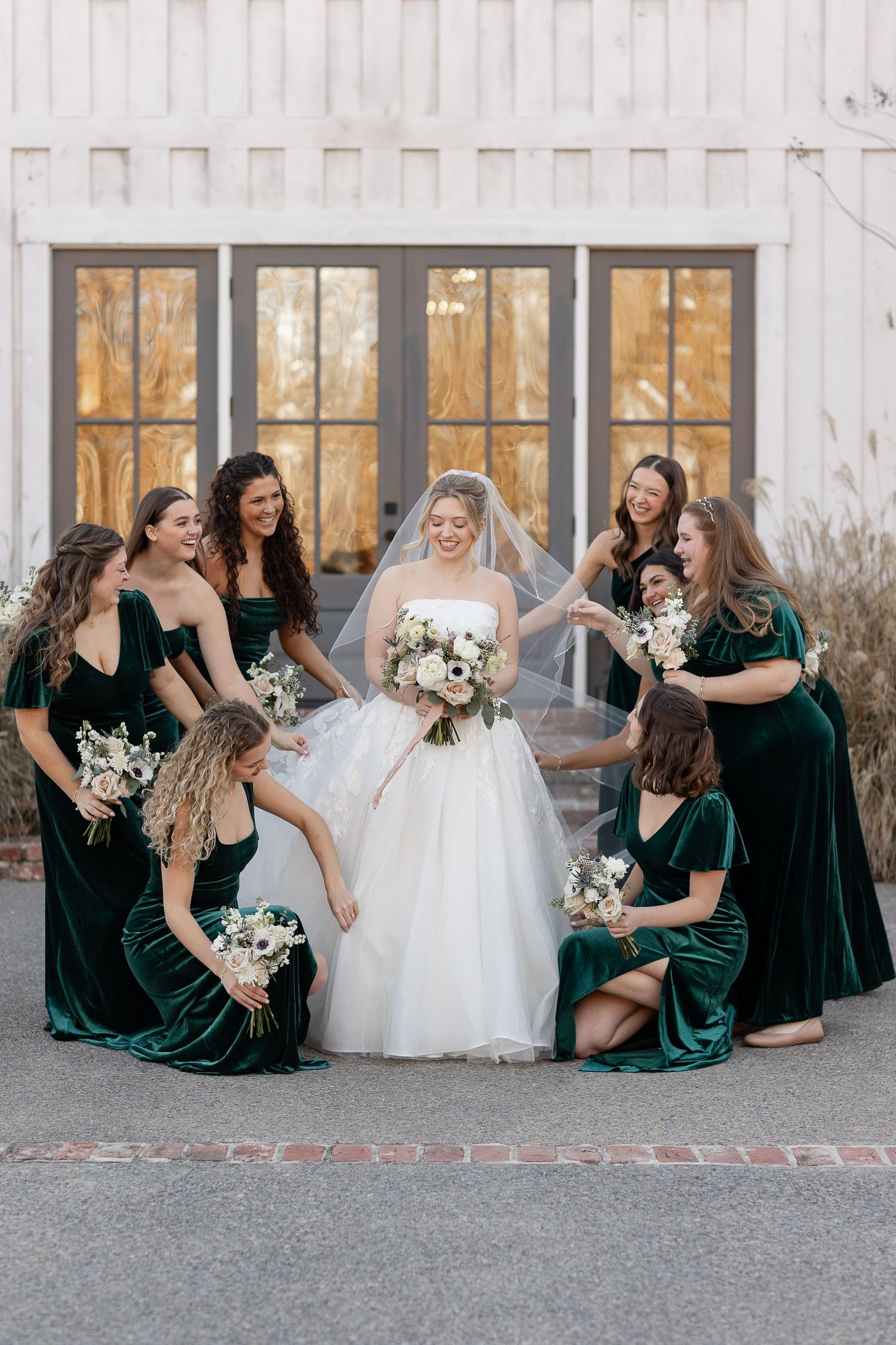 Eight bridesmaid admire a bride while they help her adjust her dress and veil. Image by Emily Joy, wedding photographer in Memphis.