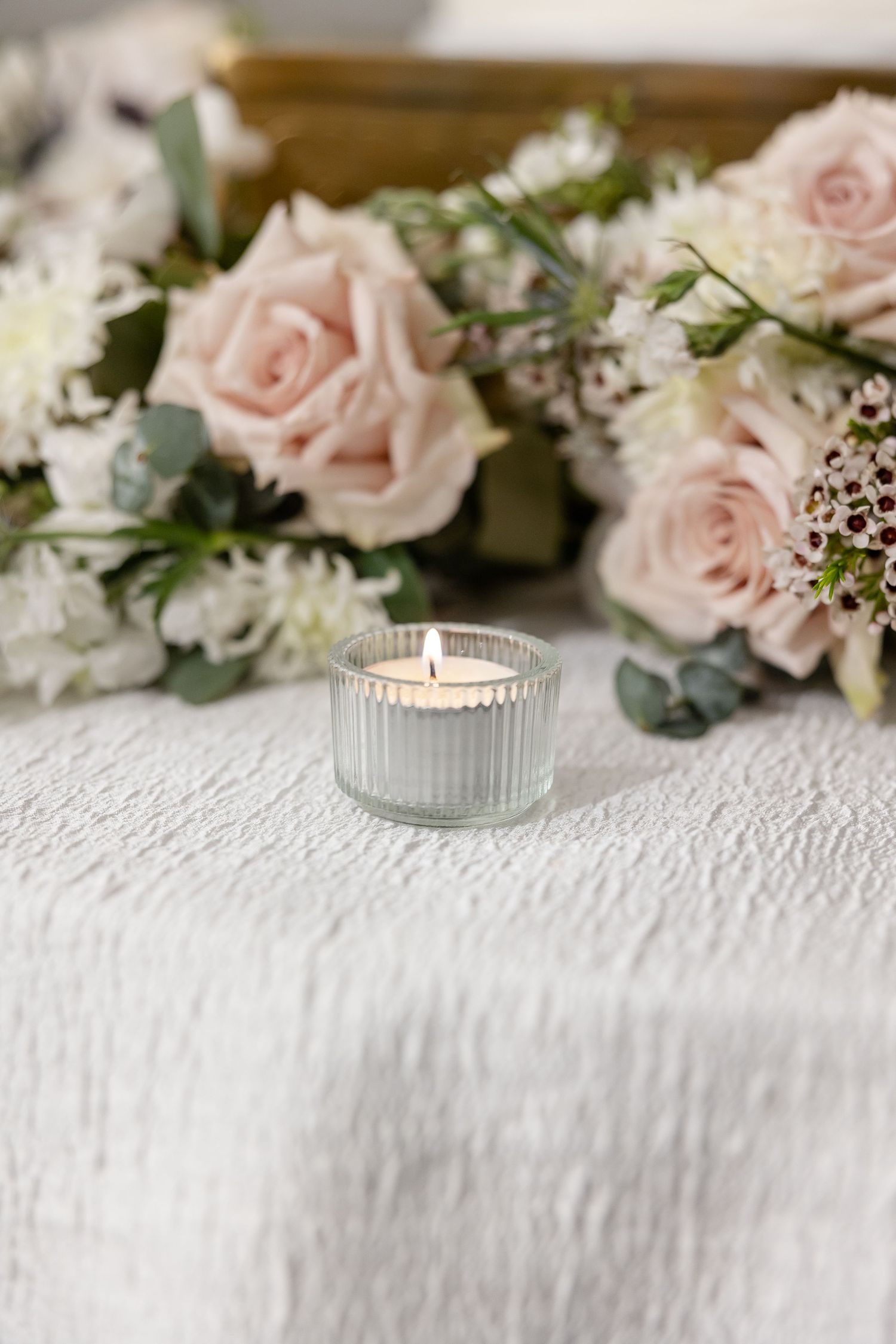 A detail shot of a burning tea light candle surrounded by pink and green florals. Image by Emily Joy, wedding photographer in Memphis.