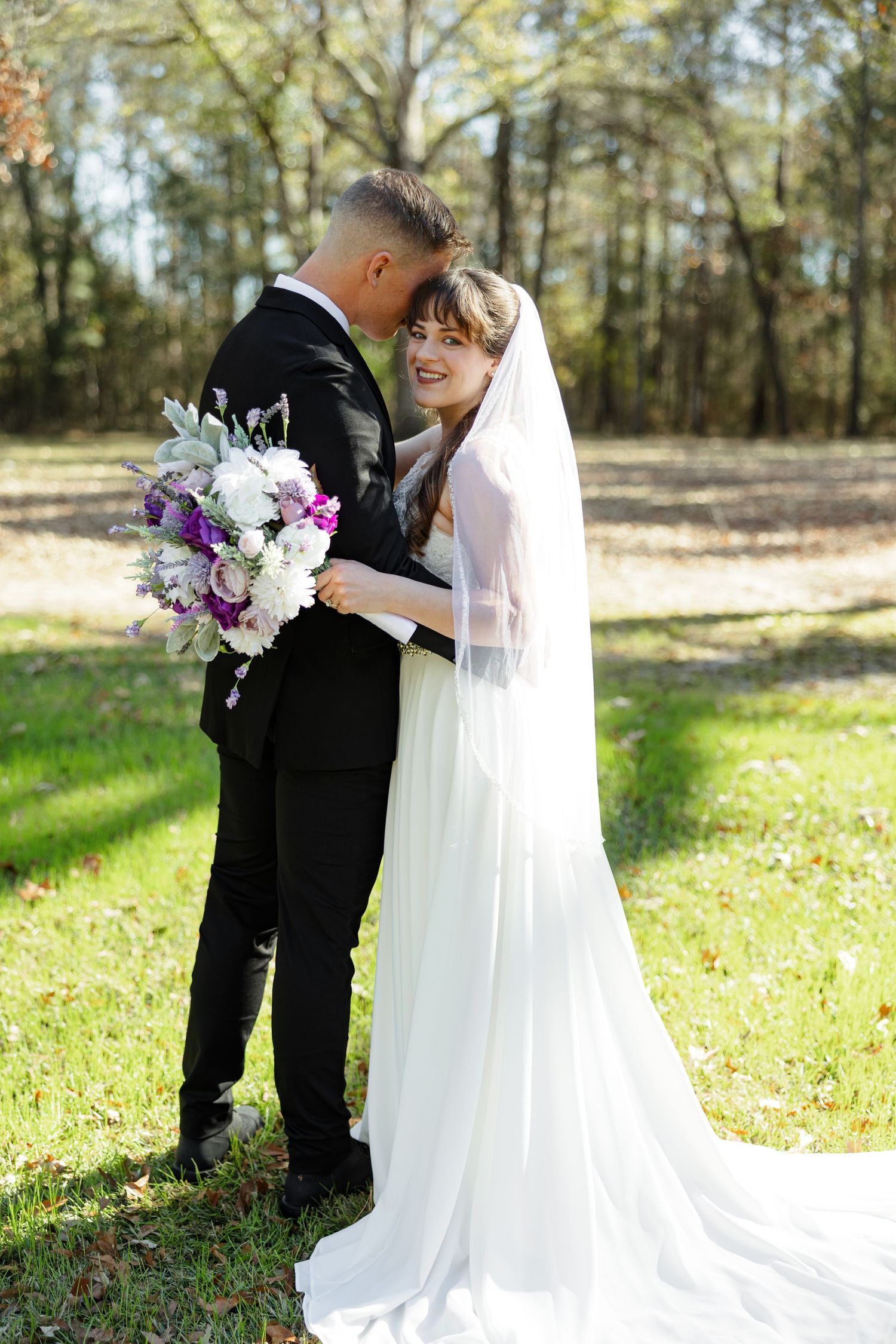 A bride and groom hugging while the bride holds her bouquet.