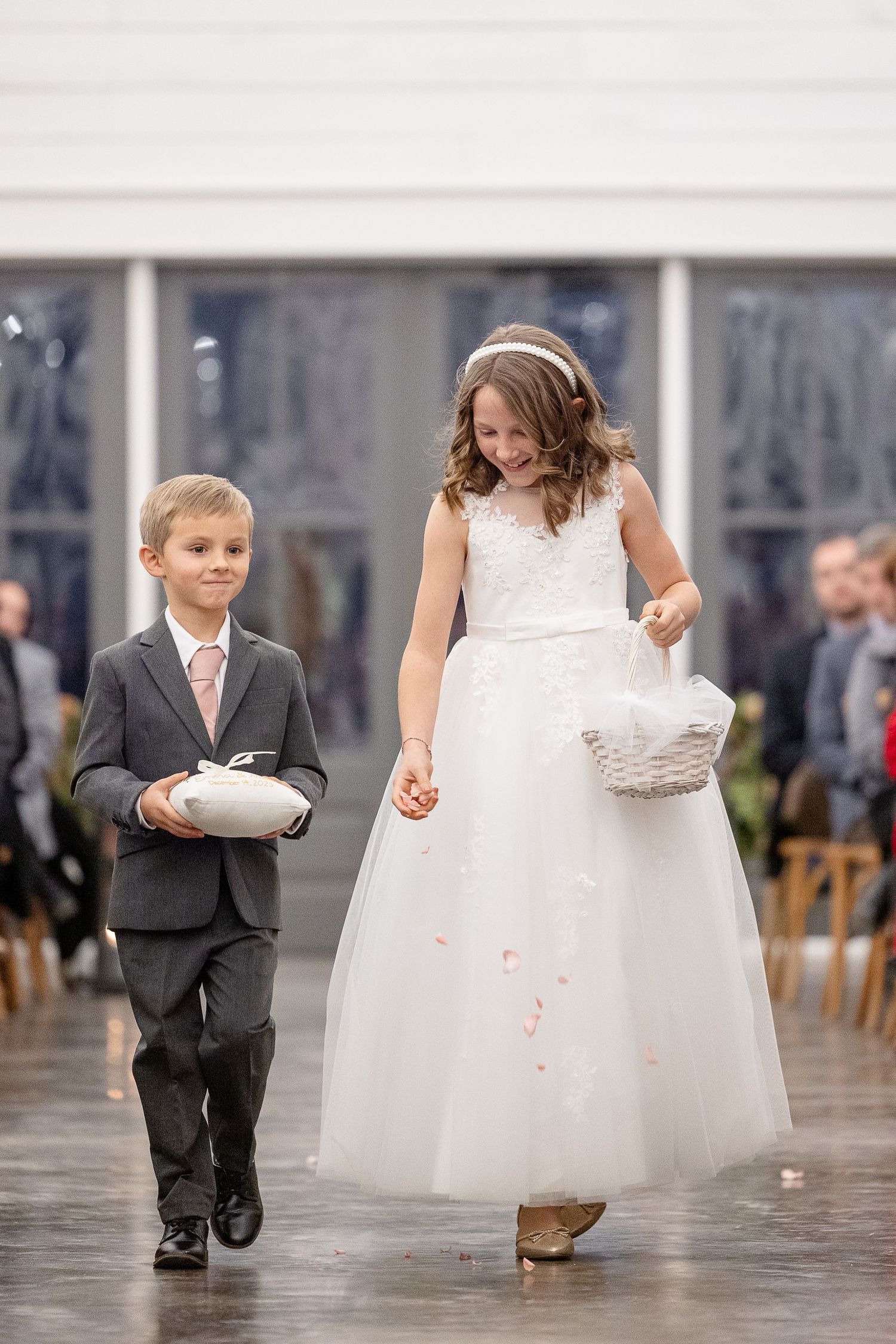 A ringbearer and a flower girl dropping rose petals smile as they walk down the aisle. Image by Emily Joy, wedding photographer in Memphis.