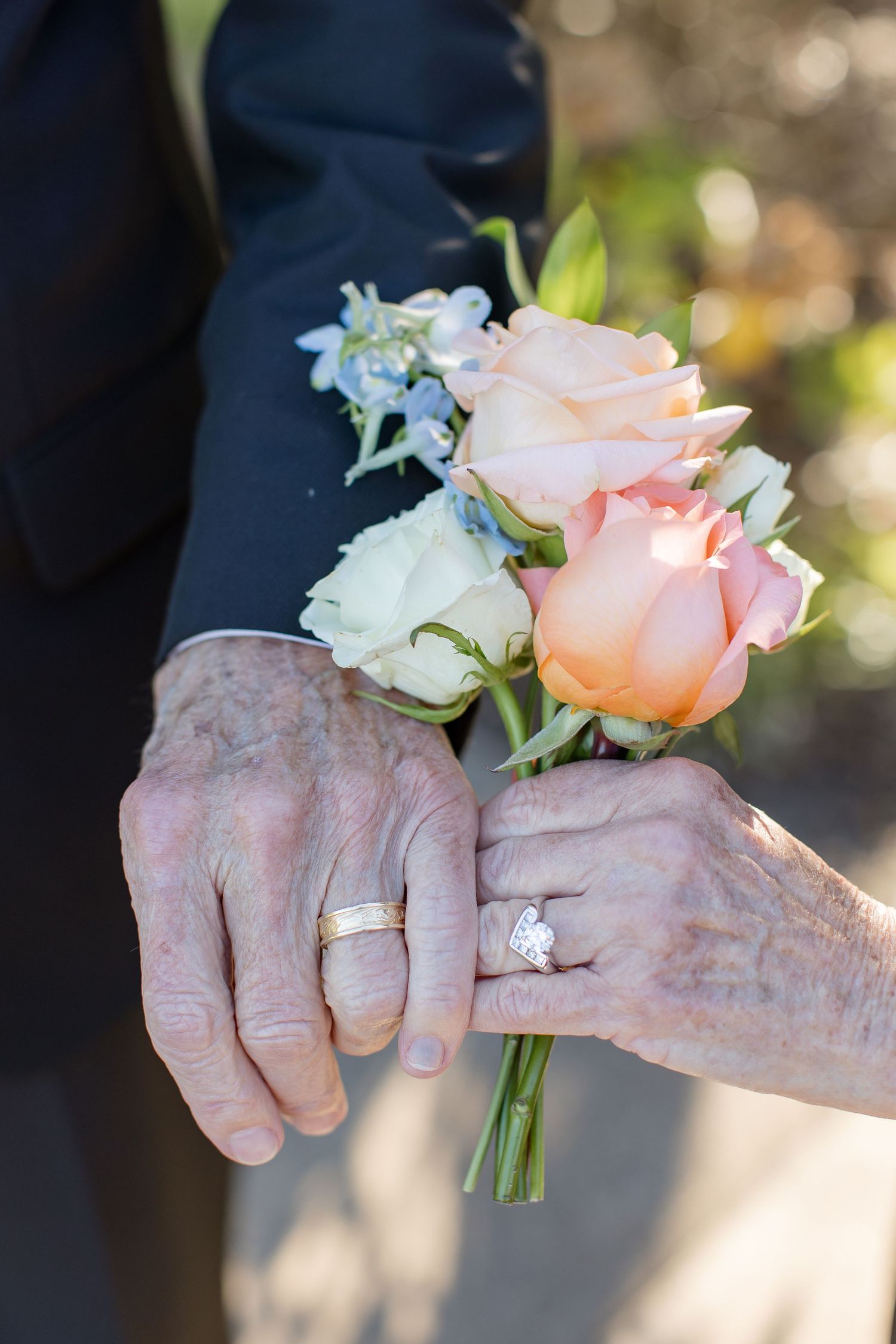 A couple with aged hands holding flowers and displaying their wedding rings; portrait by Emily Joy, wedding photographer in Memphis, TN.