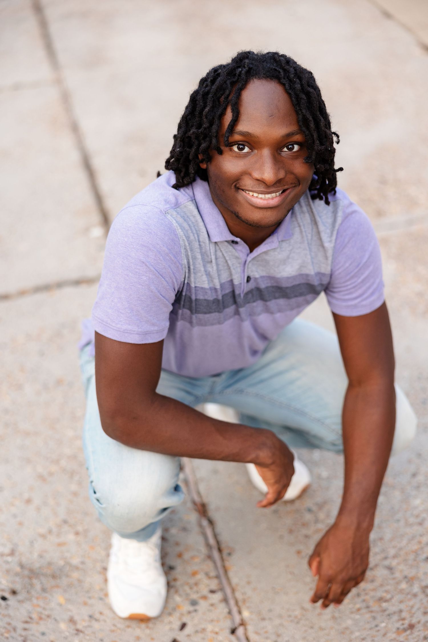 A senior boy crouches down for a smiling portrait.