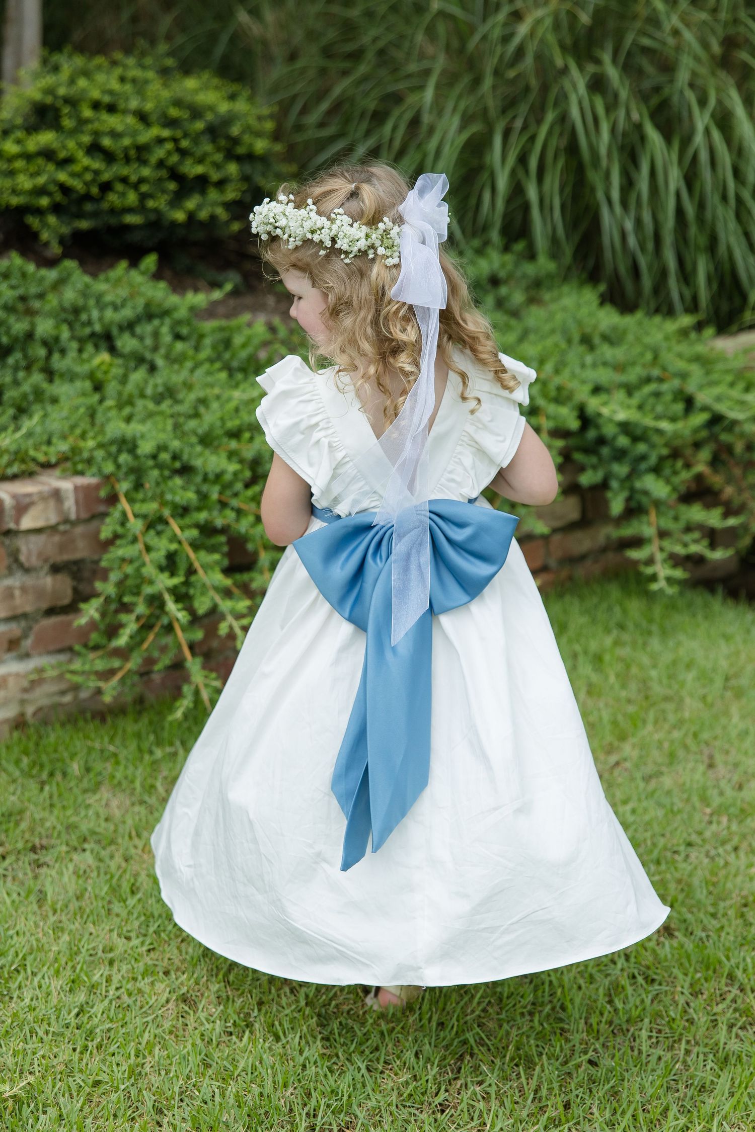 A flower girl in a white dress and a blue sash spins around in a portrait by Emily Joy Photography, wedding photographer in Memphis, TN.