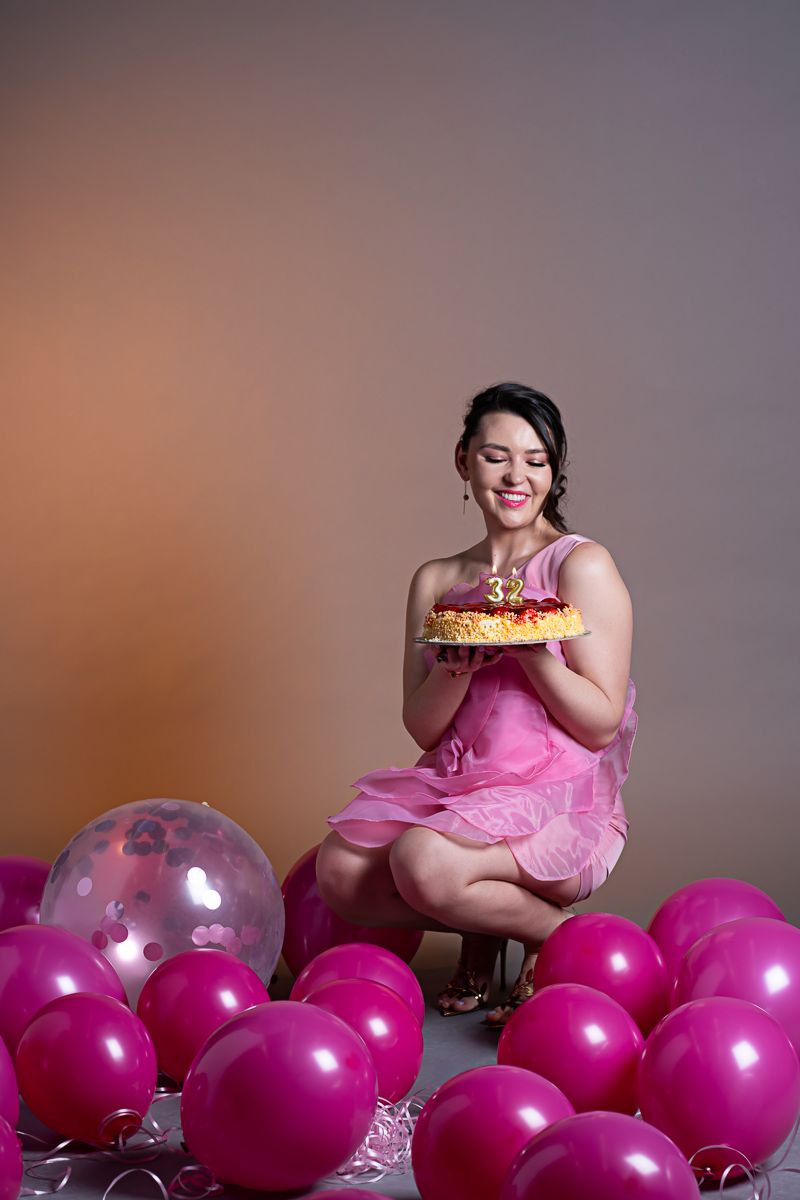 Woman celebrating her birthday with a cake and pink balloons during a Toronto studio photography session.