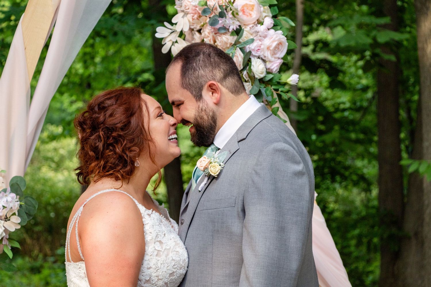 Intimate moment between couple under a floral arch during their outdoor wedding ceremony.