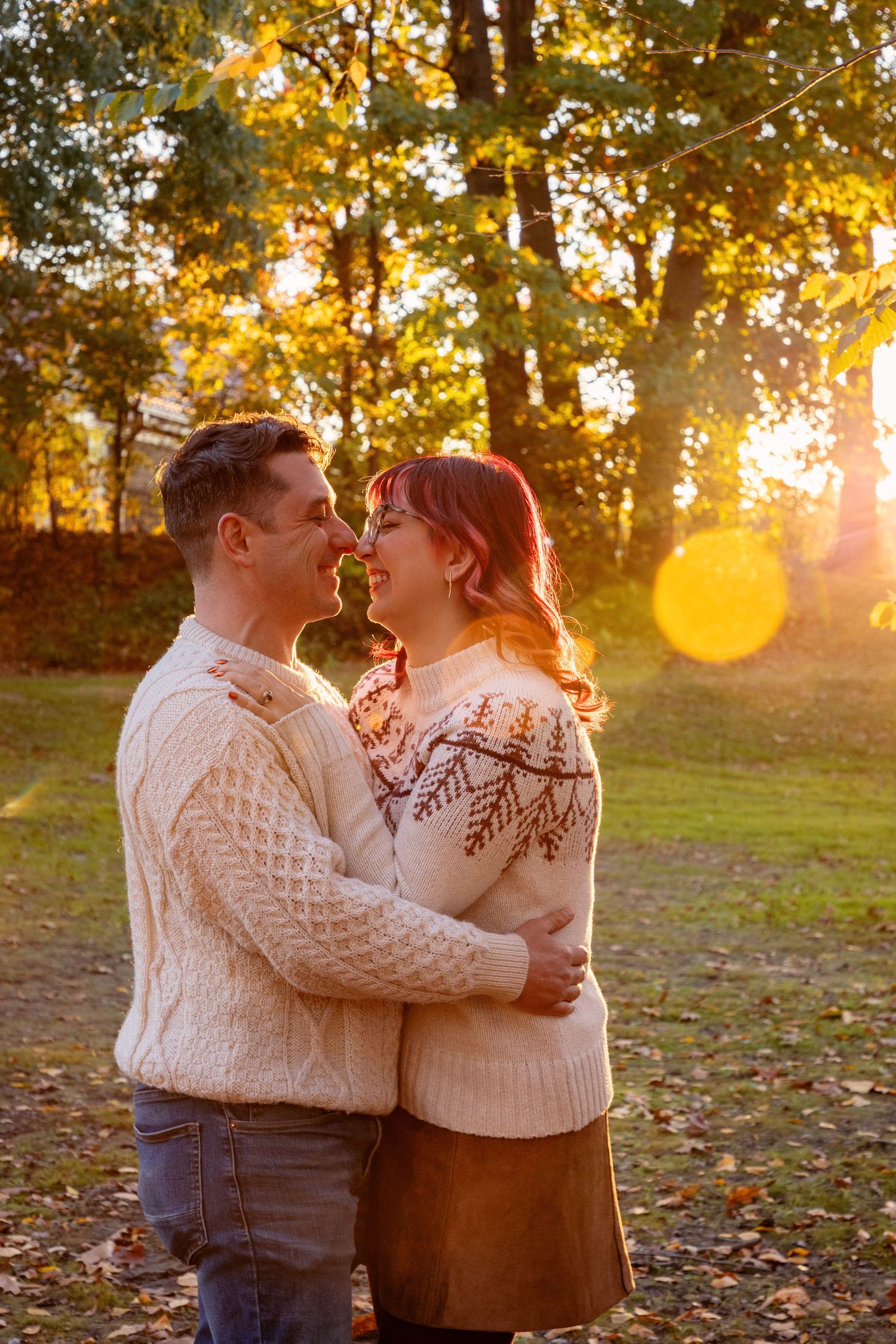 Couple in matching sweaters sharing a romantic moment during golden hour in a park.
