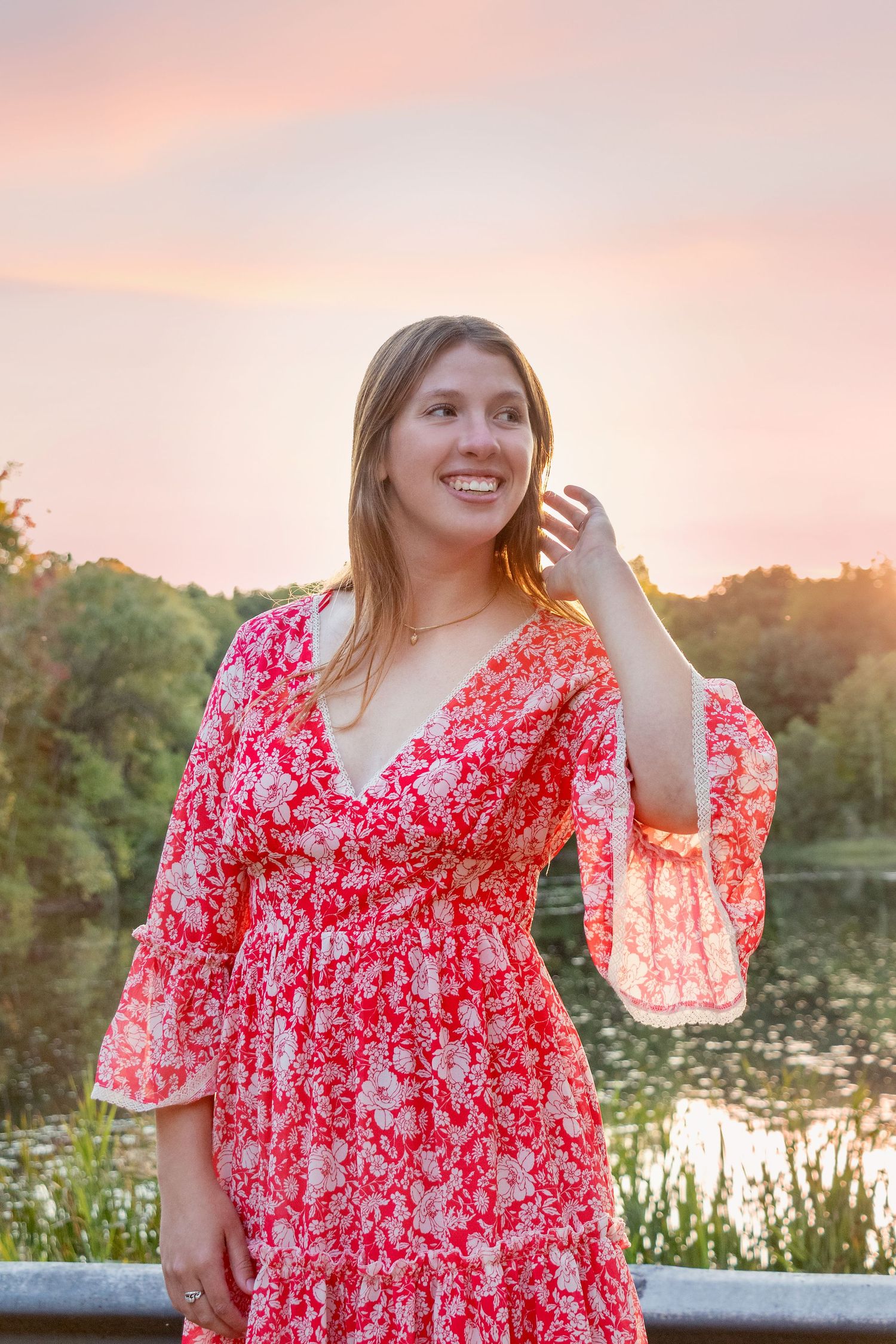 Sunset portrait session by a lake with person wearing flowing red floral dress.