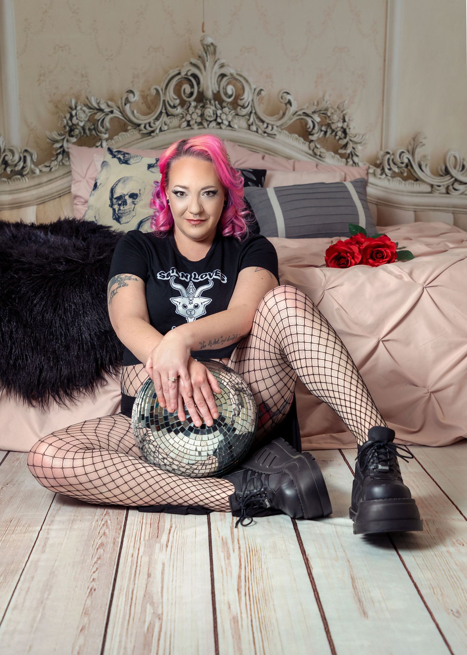 Alternative style portrait with pink hair and fishnet stockings on bedroom set.