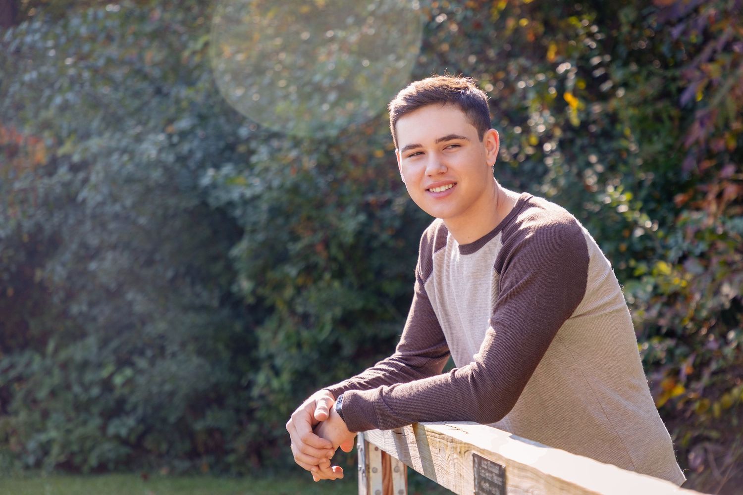 Person wearing brown vest and light colored top poses in outdoor garden setting.